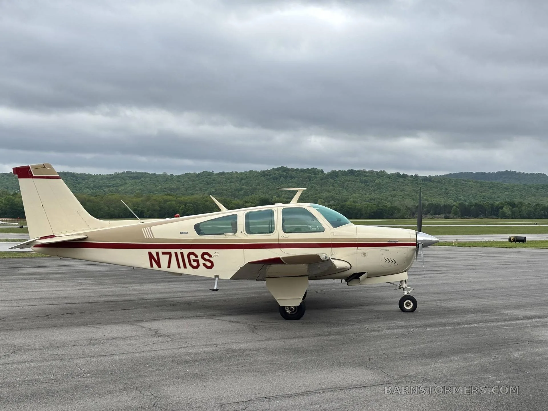 A cream and red Beechcraft Debonair N711GS parked on an asphalt ramp under a cloudy sky.