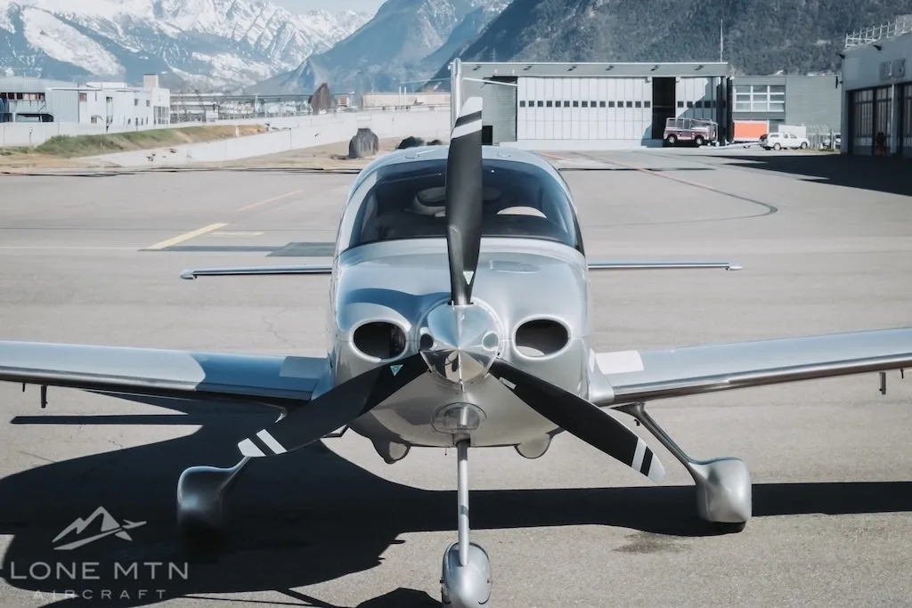 A front view of a silver Cirrus SR22 aircraft parked on an airfield.