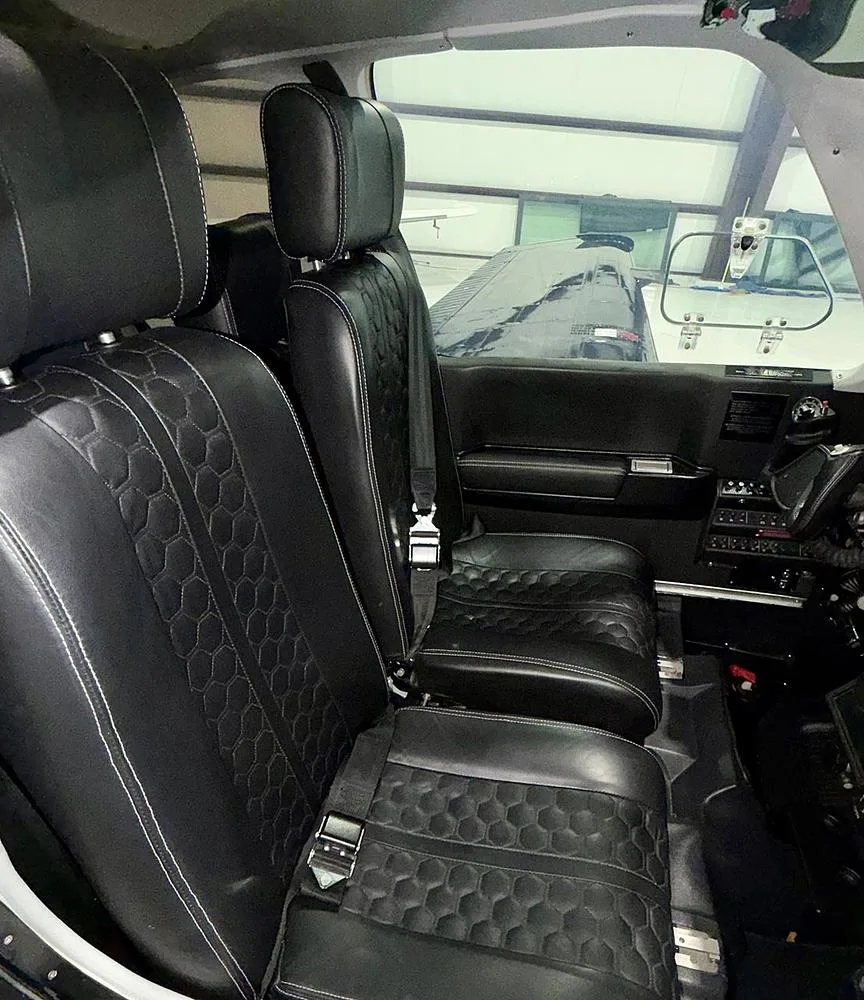 The front two black leather seats with white stitching and a hexagonal pattern in an aircraft cabin.