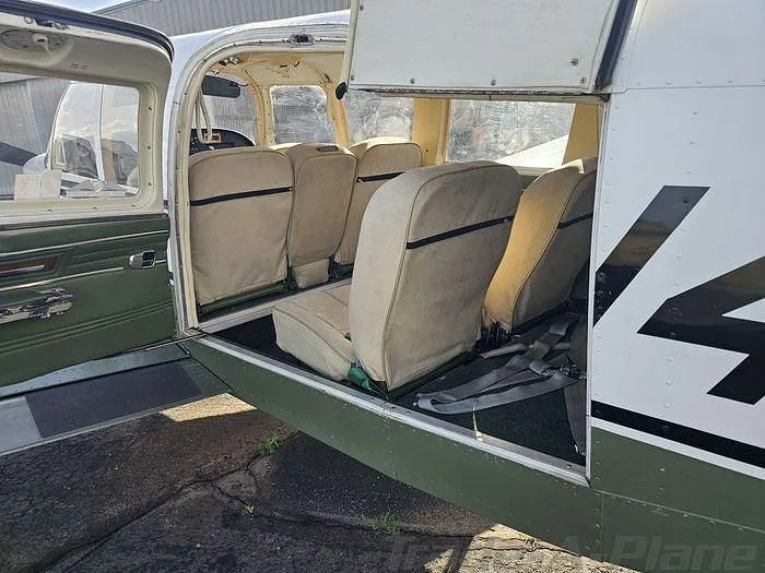 The beige fabric seats in the cabin of the white and green Piper Cherokee 180, viewed from the open door.