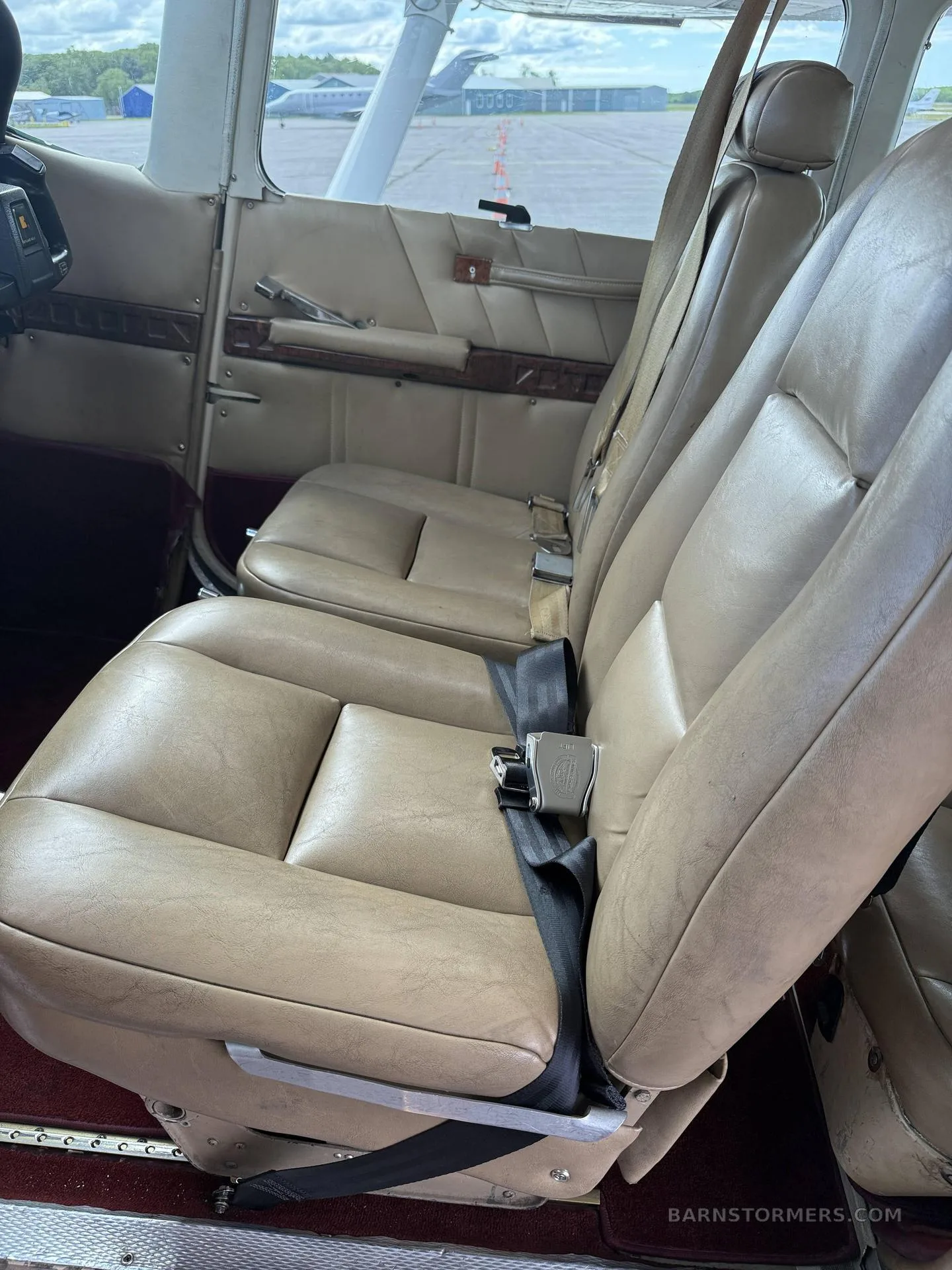 The tan leather passenger seats in the cabin of a light aircraft, with a view of the tarmac through the window.