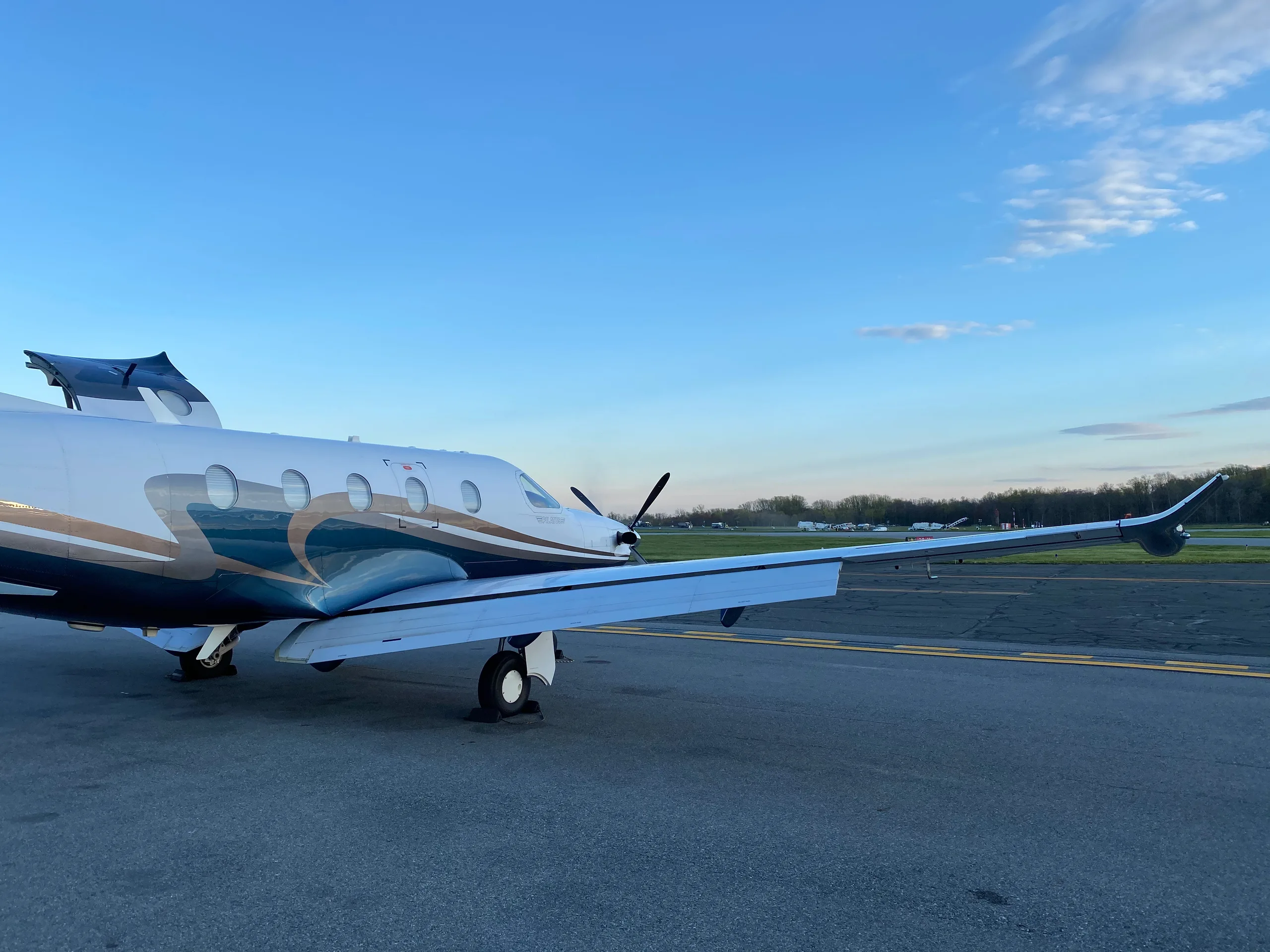 A Pilatus PC-12 aircraft is parked on the tarmac with a blue and brown paint scheme.