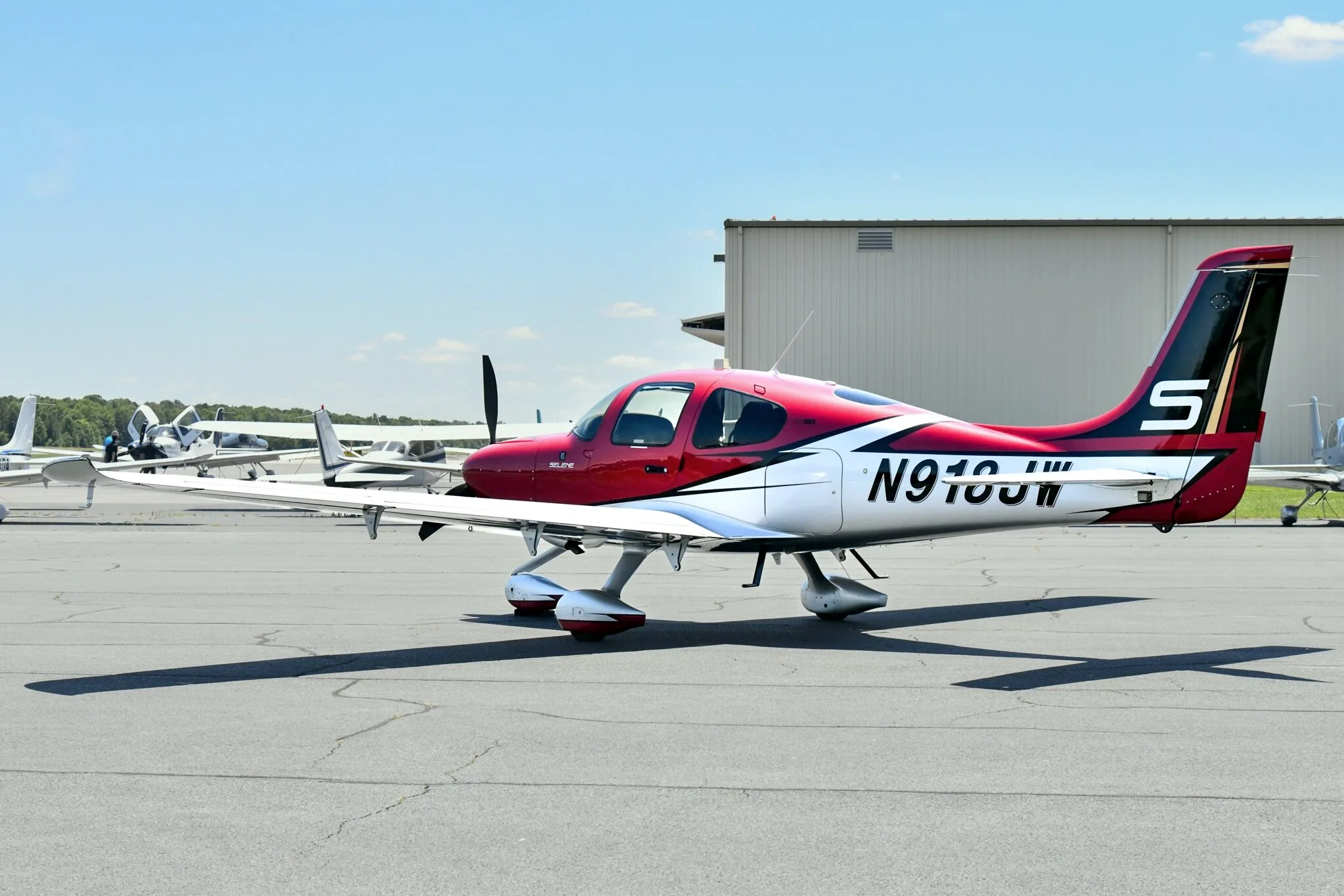 A red and white Cirrus SR22T aircraft with registration N918JW parked on an airfield, viewed from the rear-side.