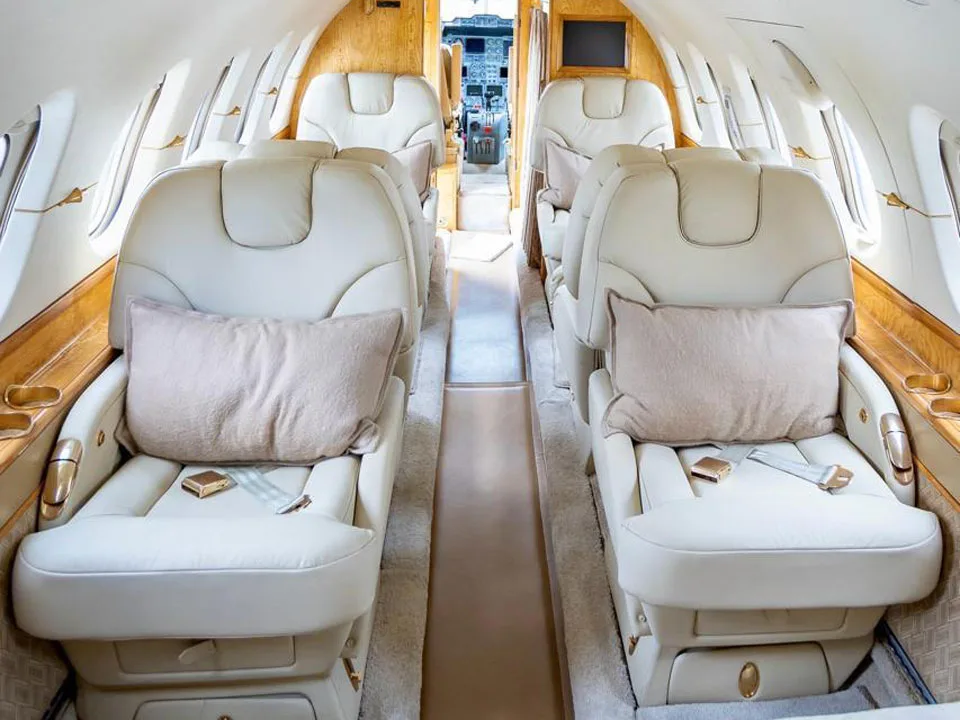 The luxurious interior cabin of a private jet with cream leather seats and wood paneling.