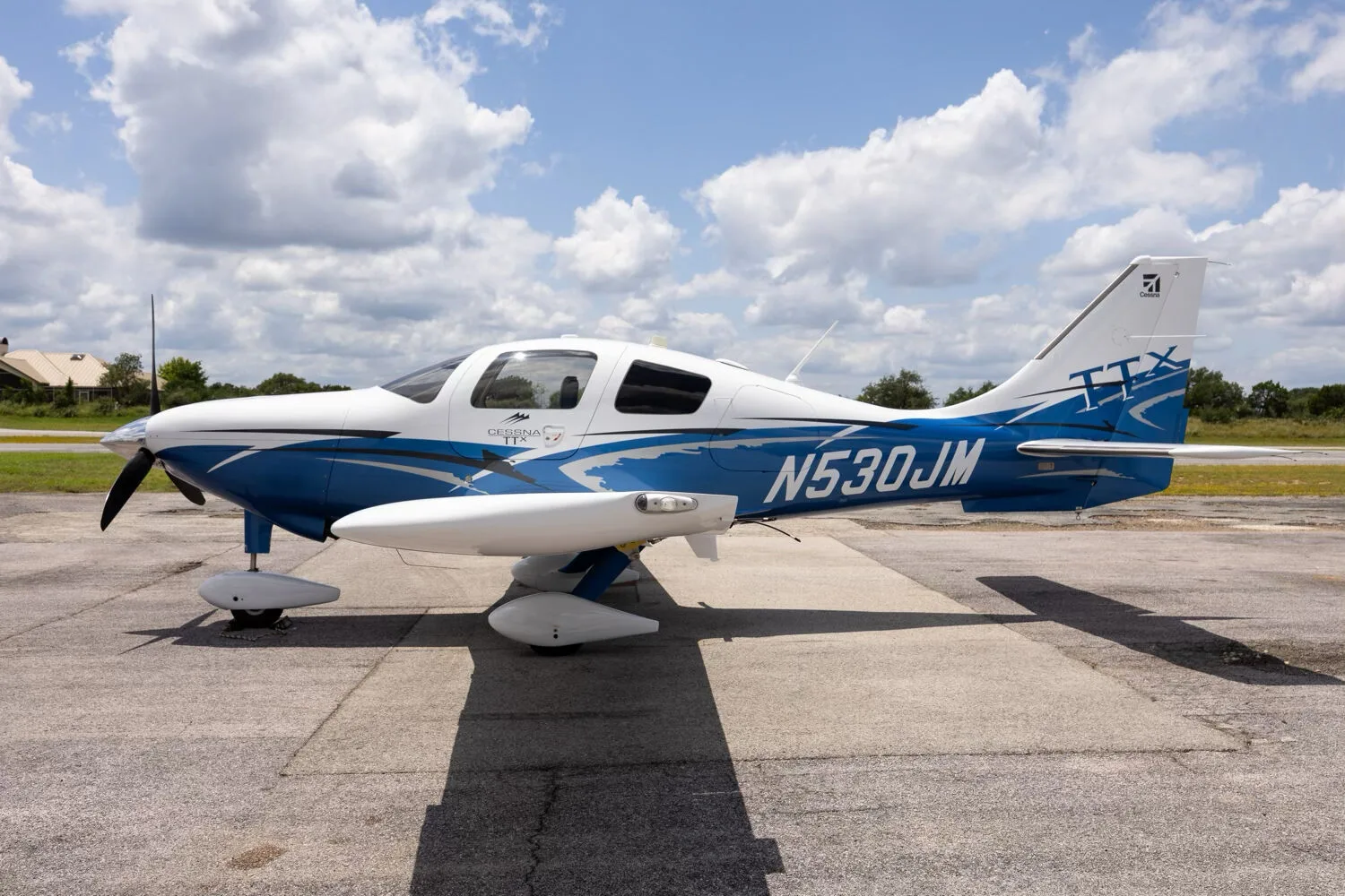 A side view of the white and blue Cessna TTX N530JM parked on a tarmac under a cloudy sky.