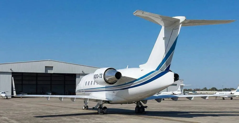 Rear-side view of the N213-TS business jet, showing its white livery with blue and grey stripes and engine.