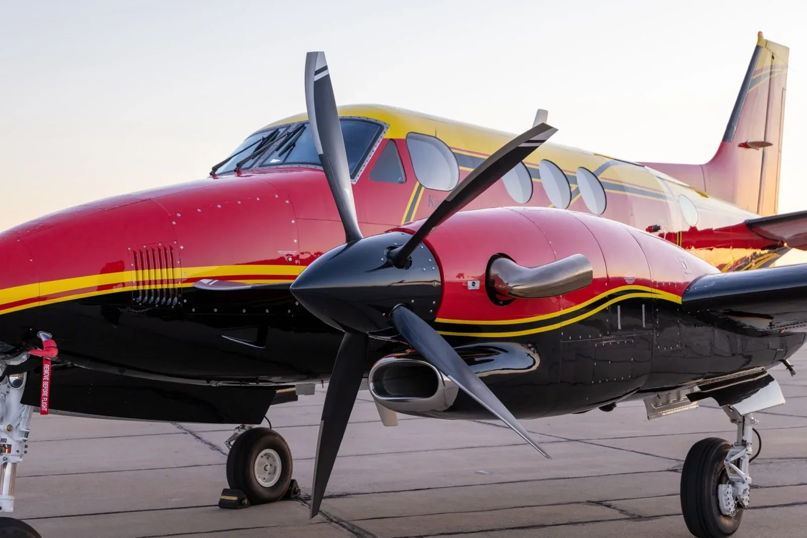 A close-up view of the right engine and propeller of a red, yellow, and black King Air C90B.