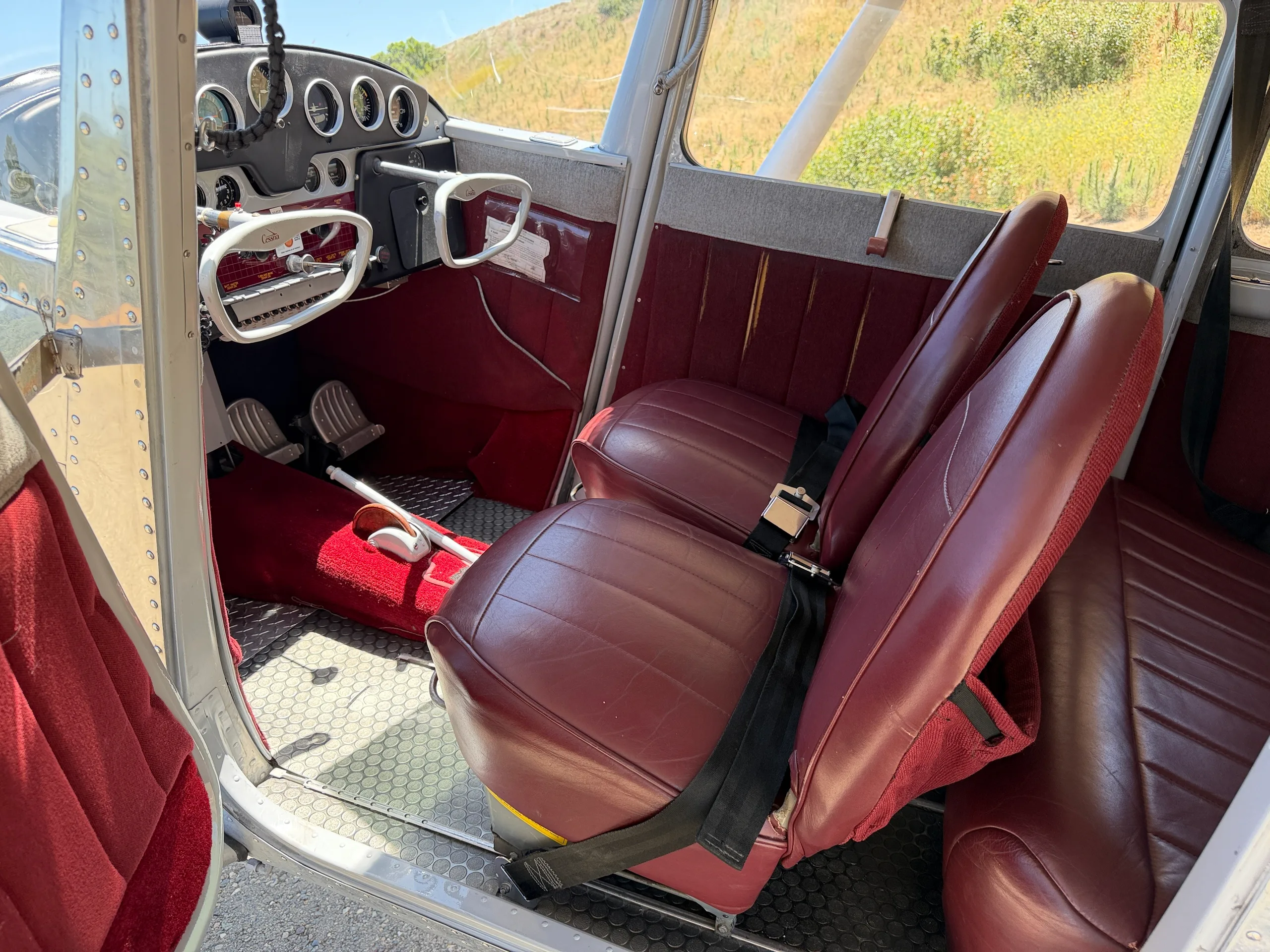 View of the red leather front seats and part of the cockpit in a polished aluminum aircraft.