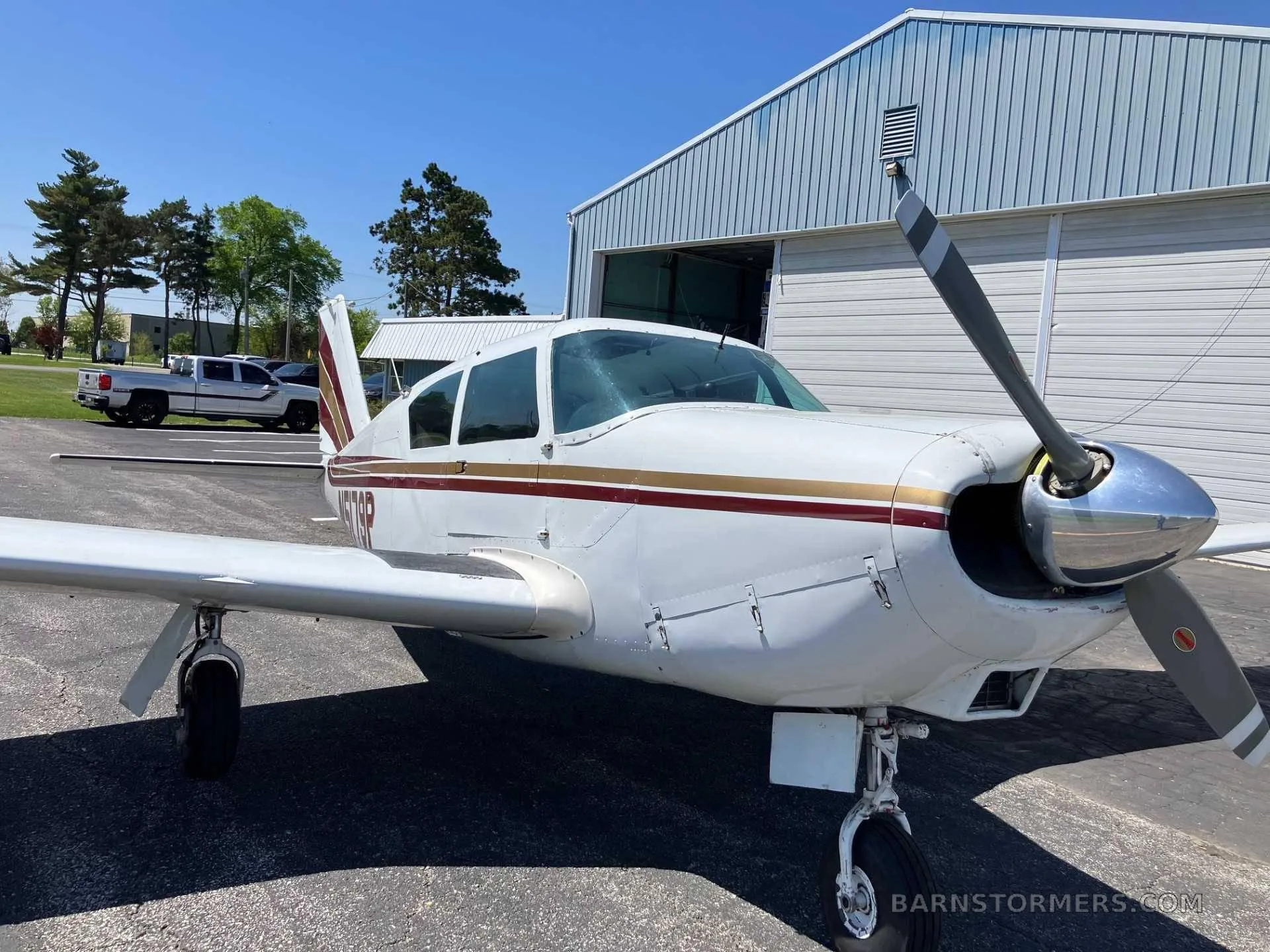 A close-up front view of a white single-engine aircraft with red and gold stripes, registration N5179P, parked on an asphalt ramp.