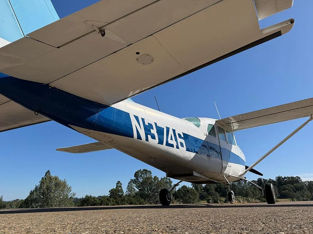 An angled low view of the white and blue single-engine aircraft N3746, showing the underside of its wing and fuselage with the registration clearly visible.