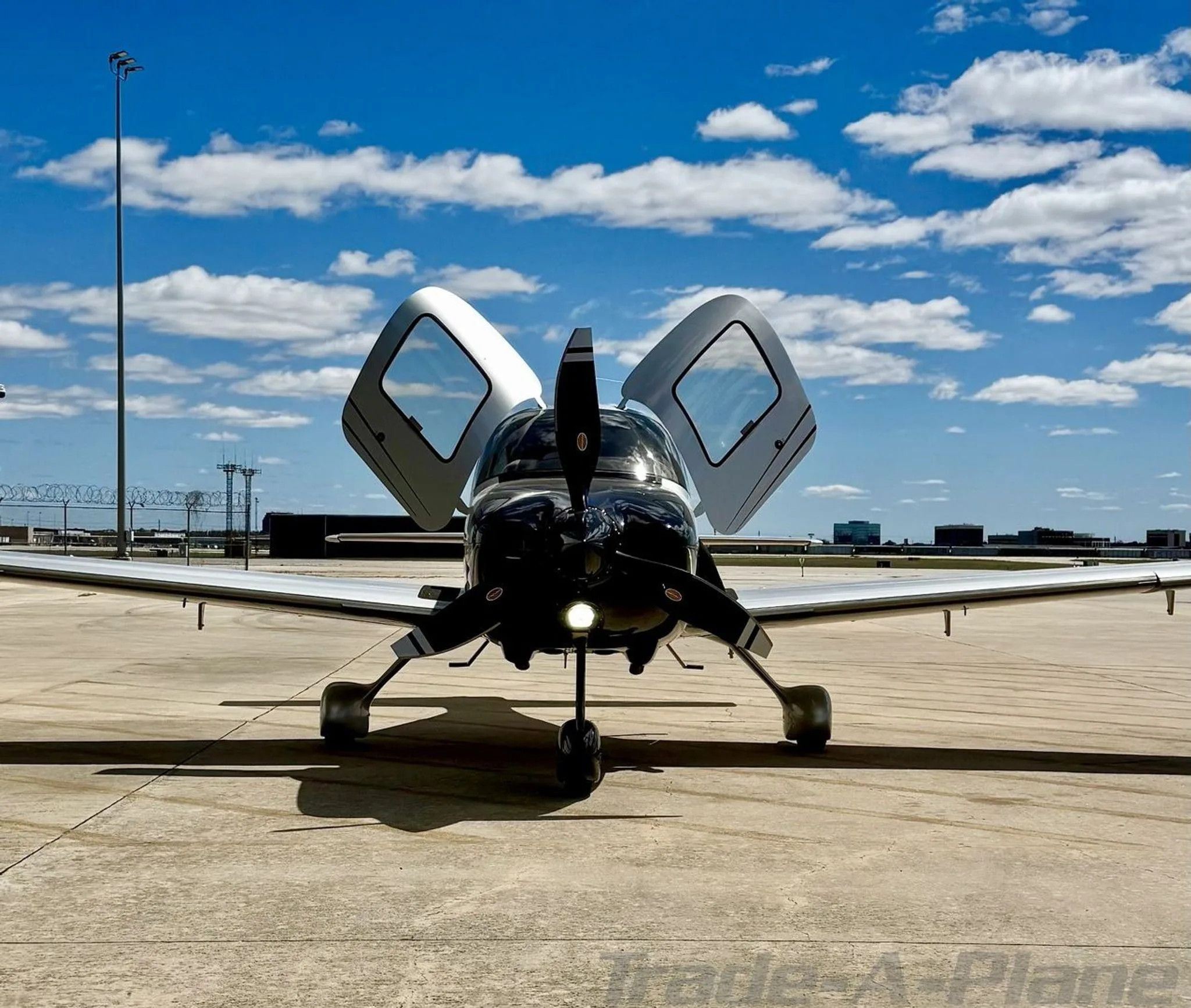 A front view of a black and silver Cirrus SR22 GTS Turbo aircraft with open doors parked on a tarmac.