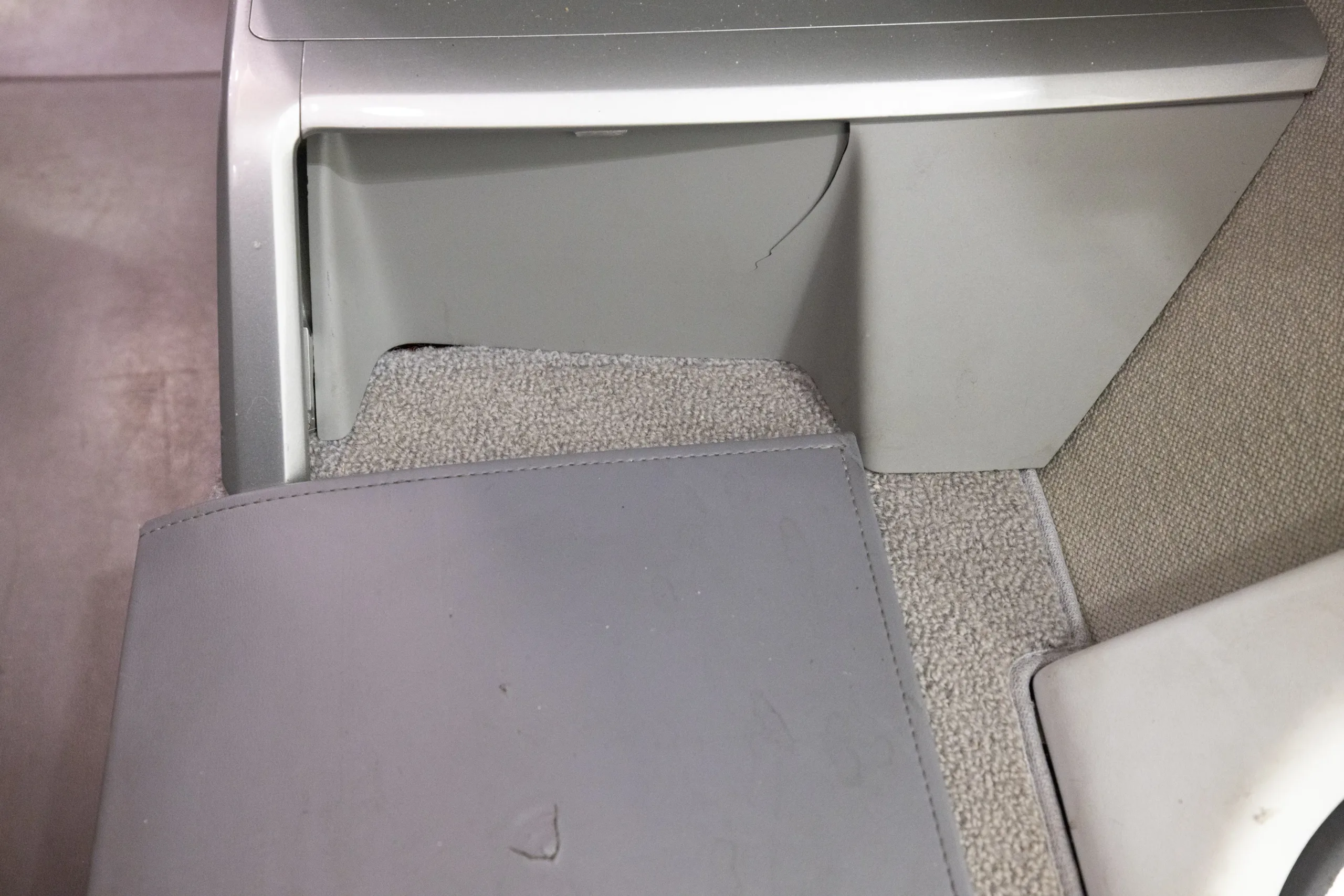 A close-up view of the light gray carpet and a small storage compartment in an aircraft cabin.