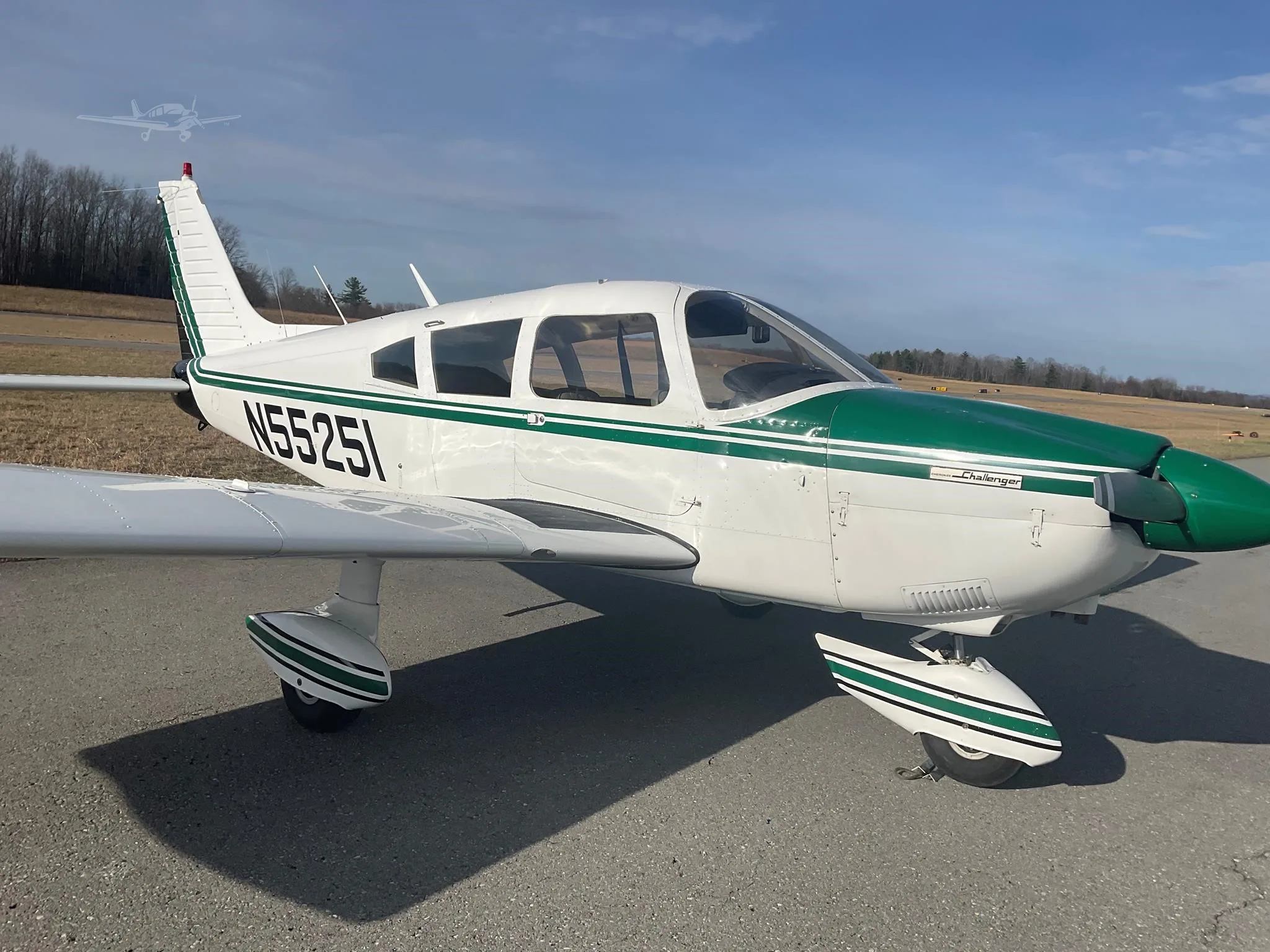 A white and green Piper Challenger aircraft is parked on an asphalt surface under a blue sky.