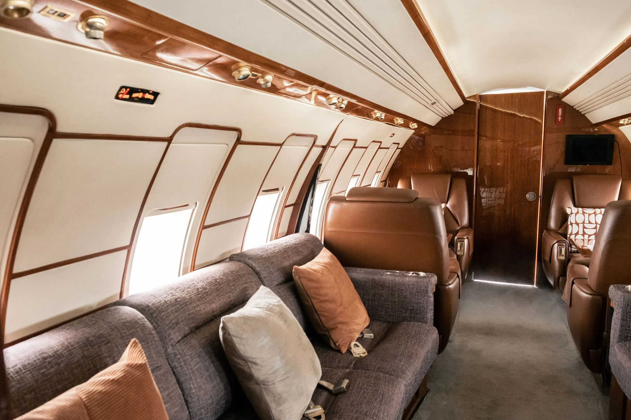 View inside a private jet cabin featuring a grey sofa with pillows and brown leather seats.