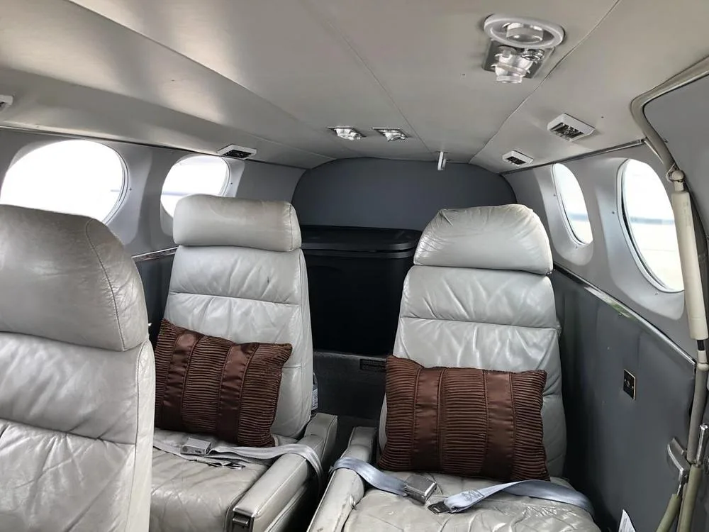 The aircraft cabin interior with two rows of light gray leather seats and brown accent pillows.