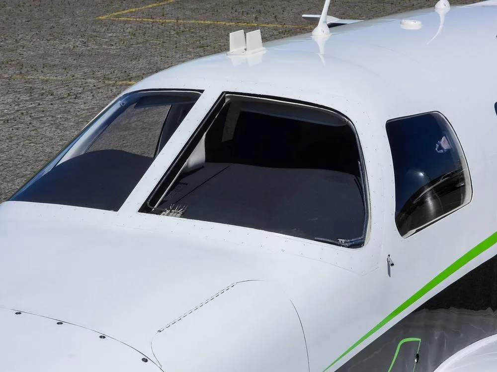 A close-up view of the cockpit windshield and front fuselage of a white aircraft with green trim.