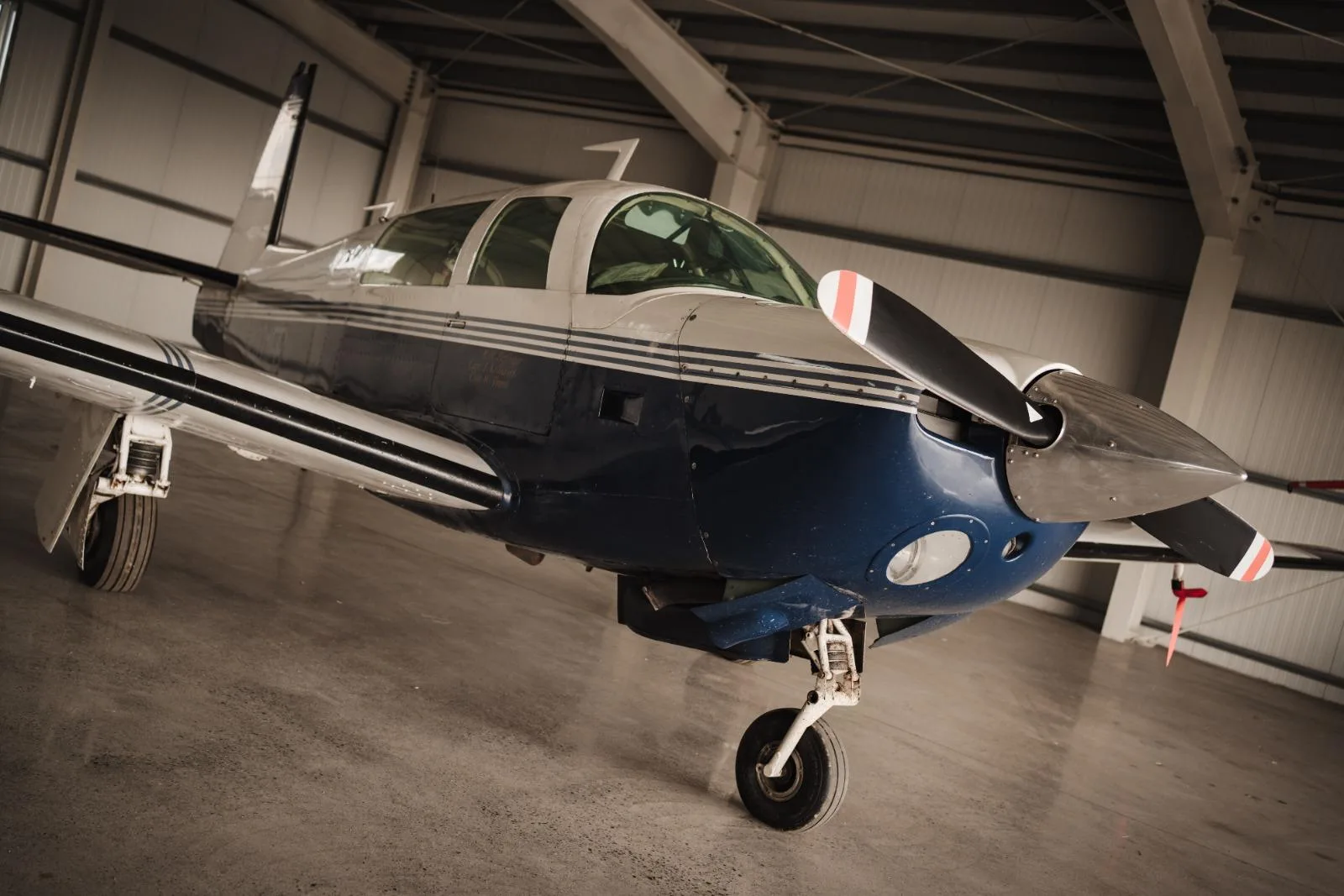A low-angle view of the front-right side of a blue and white single-engine aircraft inside a hangar.