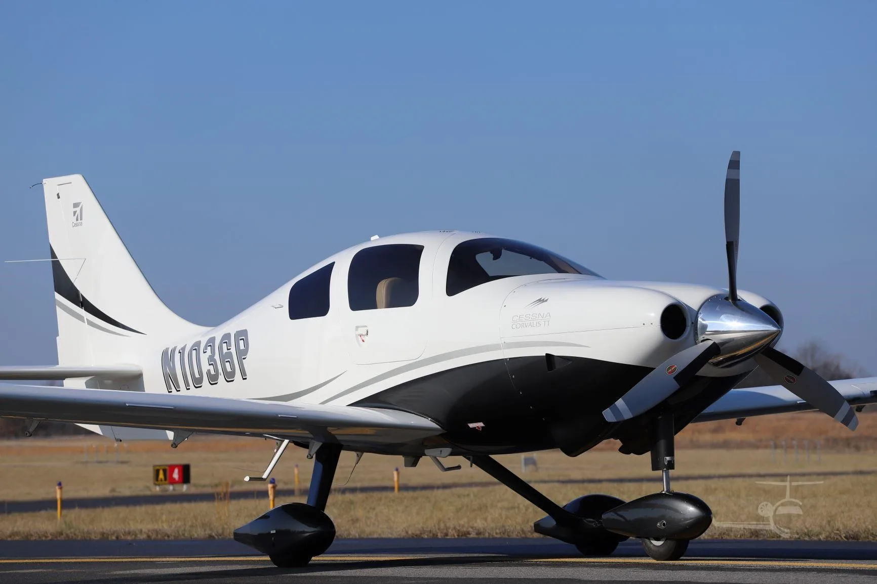 A white and black Cessna Corvalis TT (N103GP) with a three-blade propeller, parked on an airfield, viewed from the front-right.