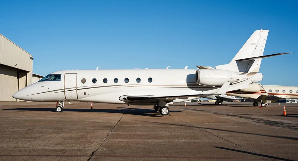 A side view of a white Gulfstream G280 business jet with gold and black stripes, registration N280LT, parked outside a hangar.