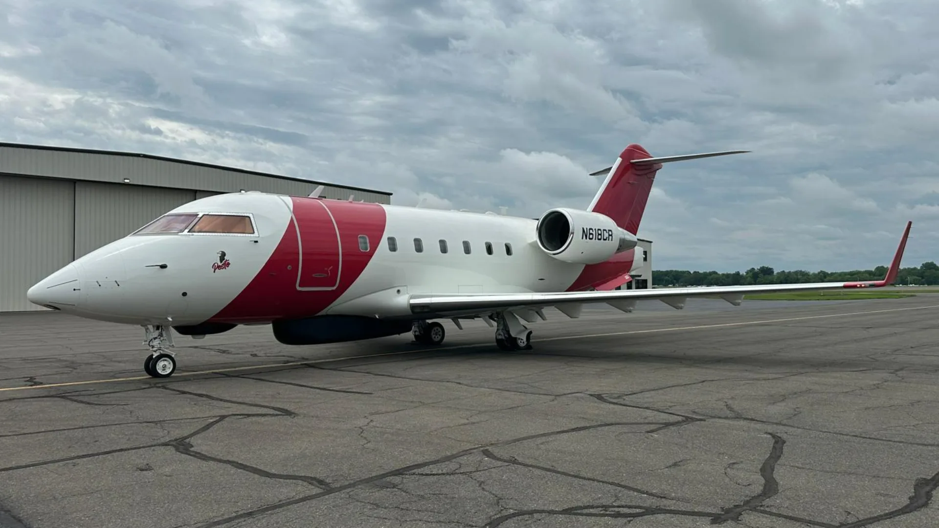 A white and red Bombardier Challenger 604 aircraft, N618CR, parked on an tarmac with hangars in the background.