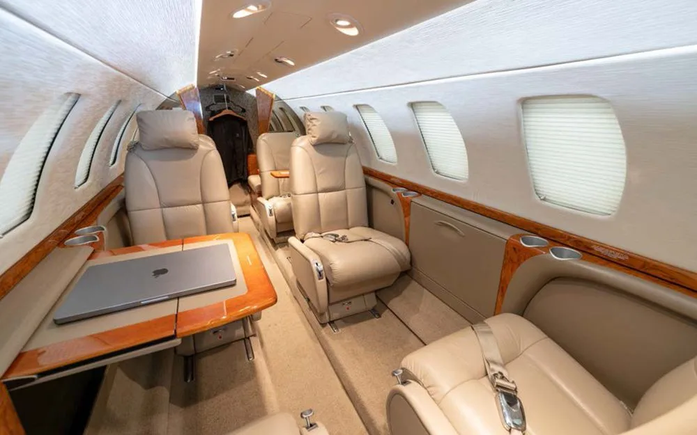 The luxurious beige leather interior of a private jet cabin with a laptop on a fold-out table.
