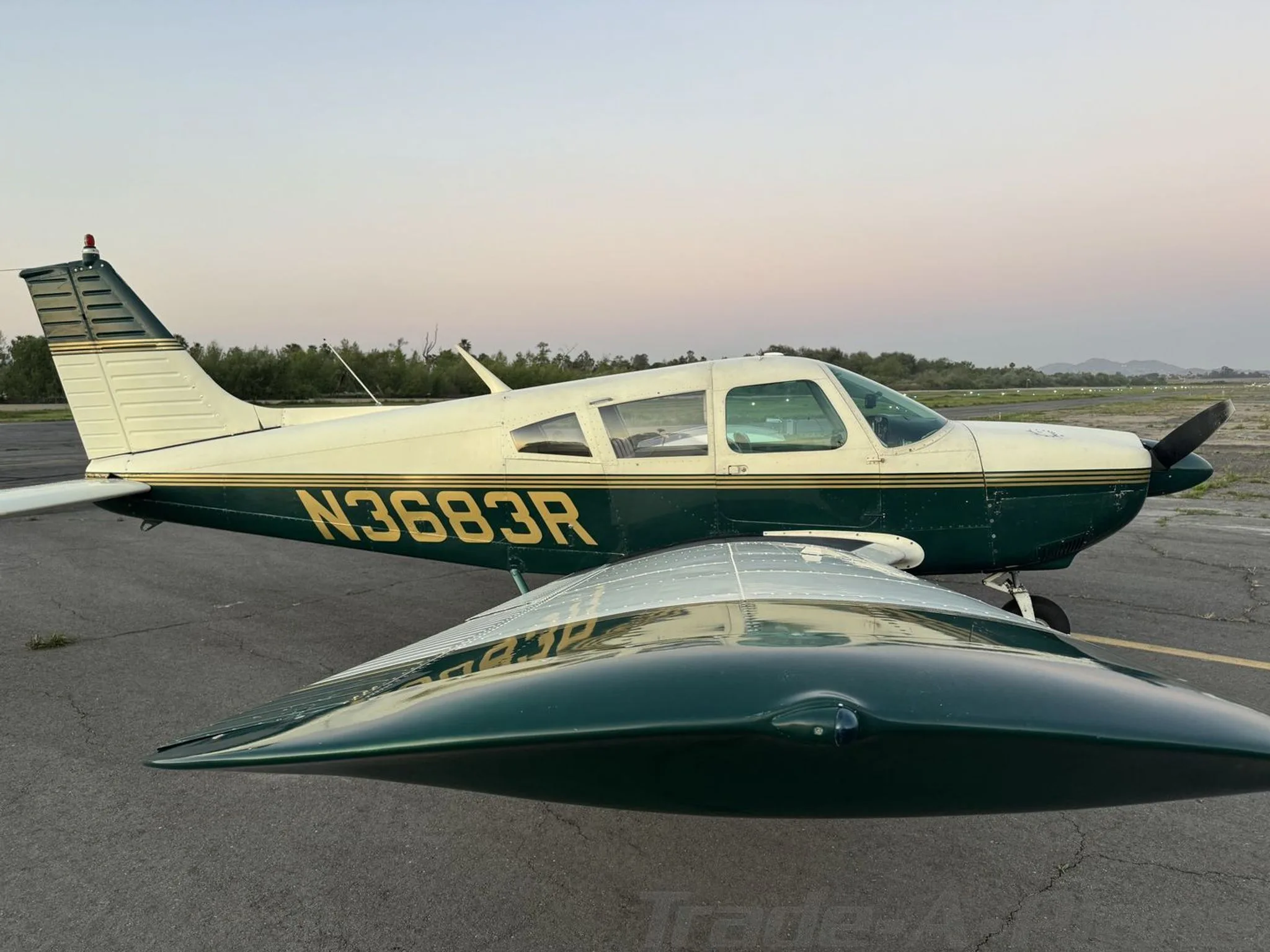 A side view of the N3683R aircraft, painted in green and white with gold stripes, on an airfield at dusk.