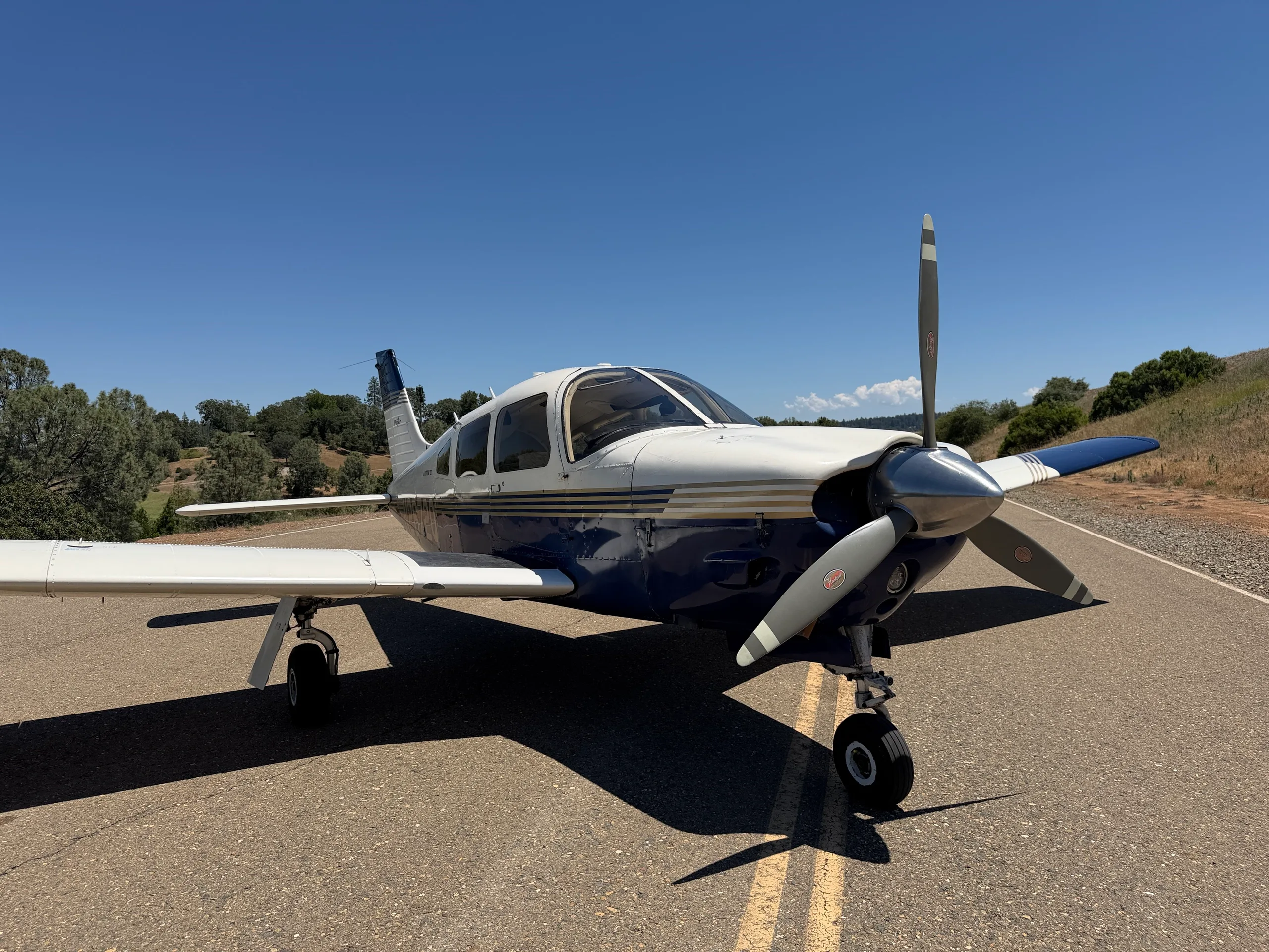 A low-angle front view of the white and blue Piper Arrow III aircraft, tail number N2672Q, parked on an asphalt surface.