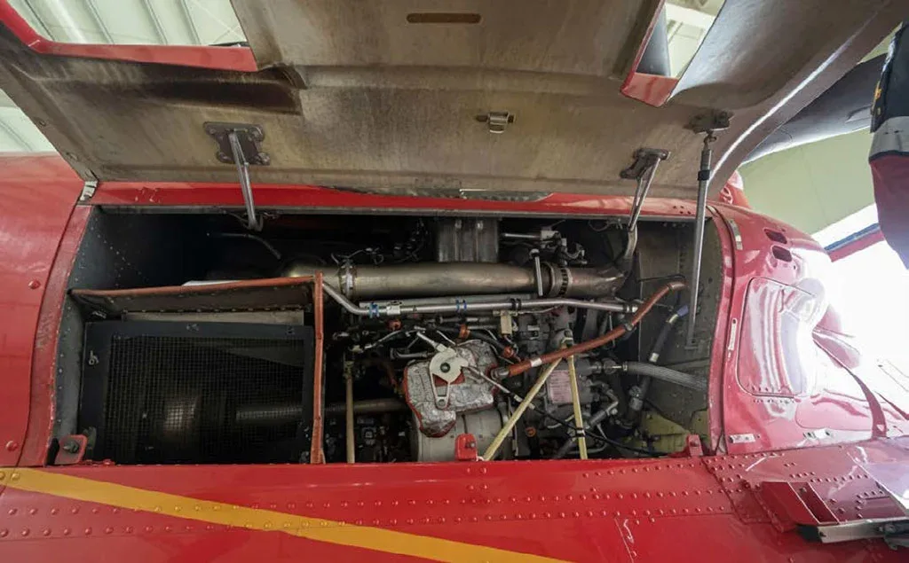 The engine compartment of a red helicopter is open, revealing the internal machinery.