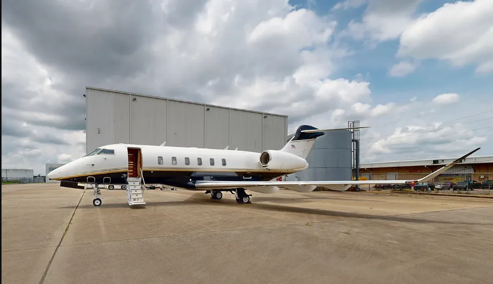 A white and black private jet with an open door and stairs parked on a tarmac next to a large building.