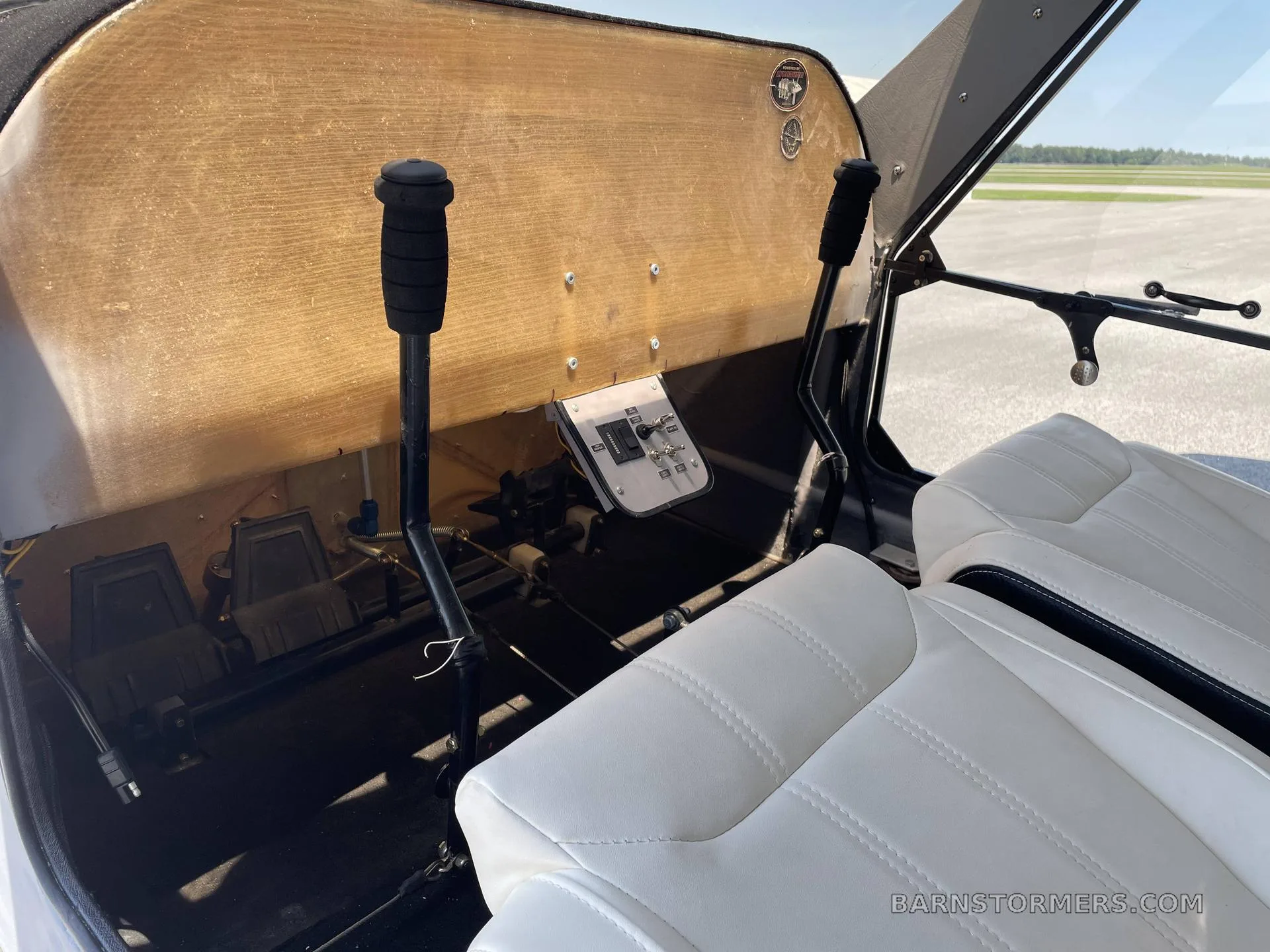 The simple cockpit features a wooden instrument panel, two control sticks, and white seats.