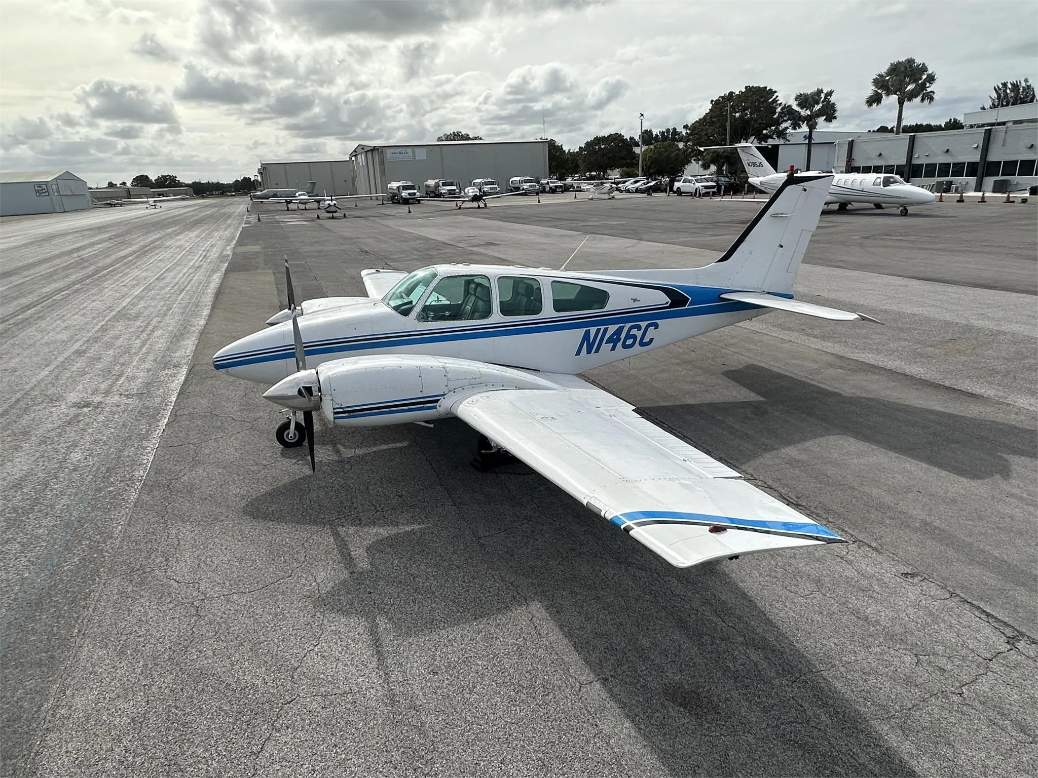 A white and blue twin-engine aircraft, N146C, parked on an airport tarmac under a cloudy sky.