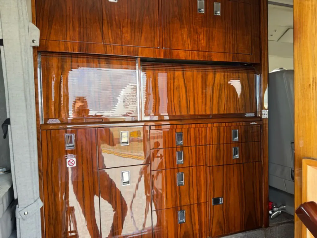 Close-up of highly polished dark wood cabinetry with silver handles inside a business jet cabin.