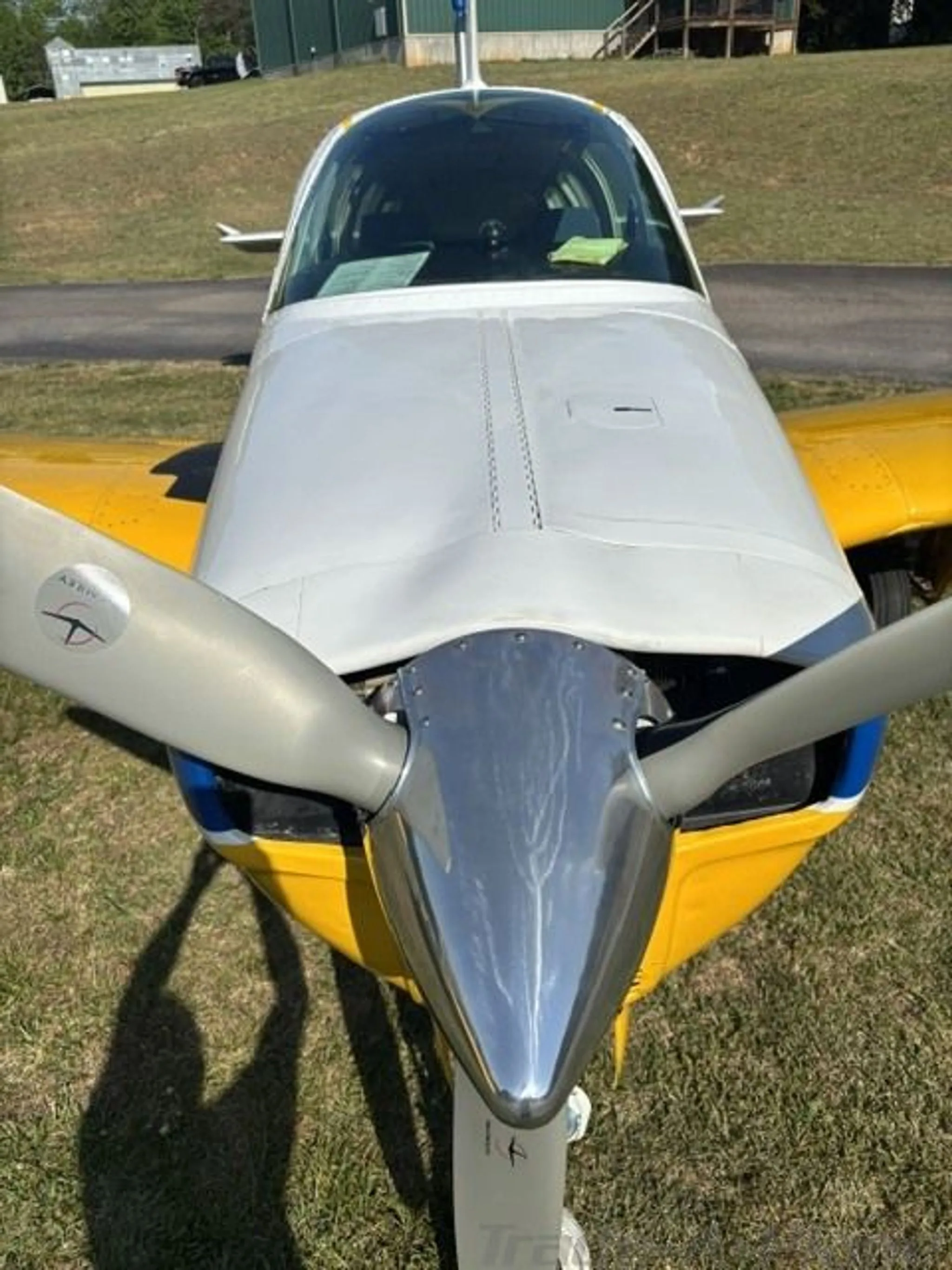 Head-on view of the propeller and nose of a yellow and white Beechcraft Bonanza 36 on grass.