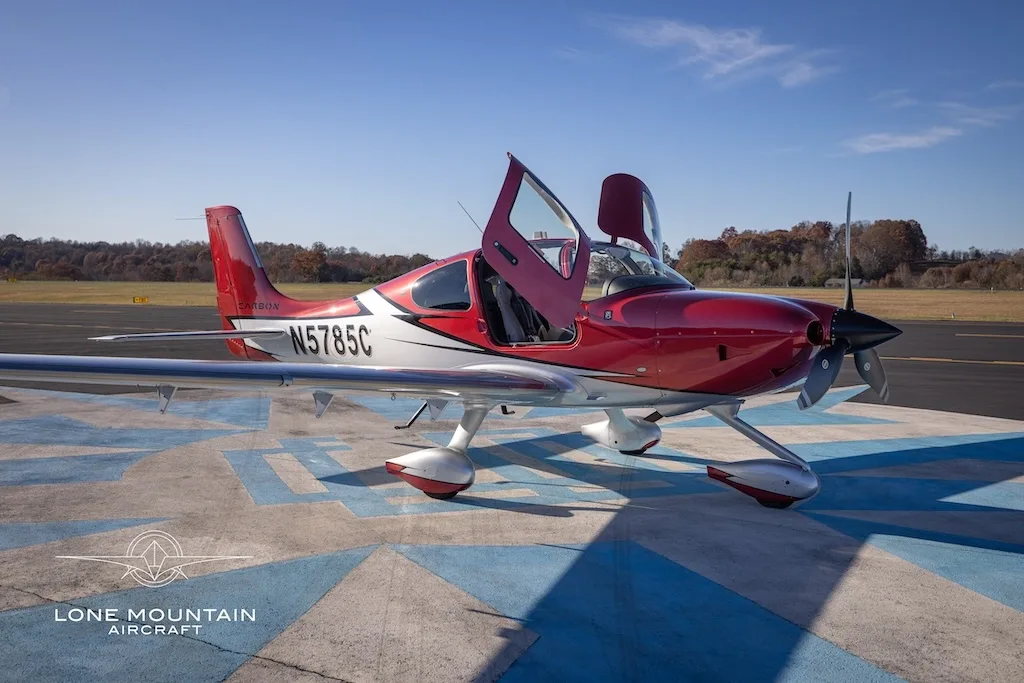 A red and white Cirrus SR22 aircraft with registration N5785C parked on an airfield with its doors open.