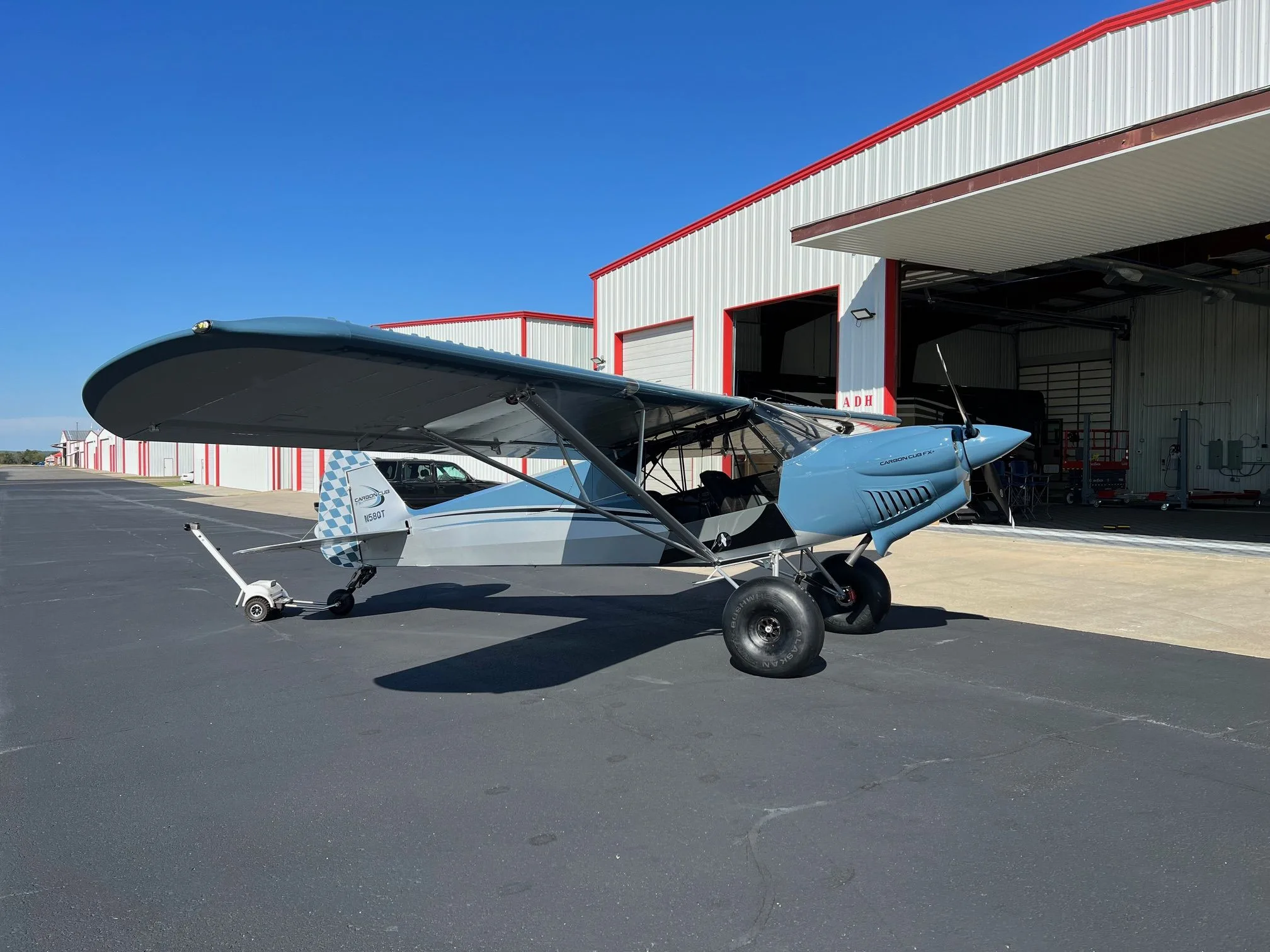 A blue and grey Carbon Cub FX-3 aircraft with registration N58QT parked outside a hangar on an airfield.