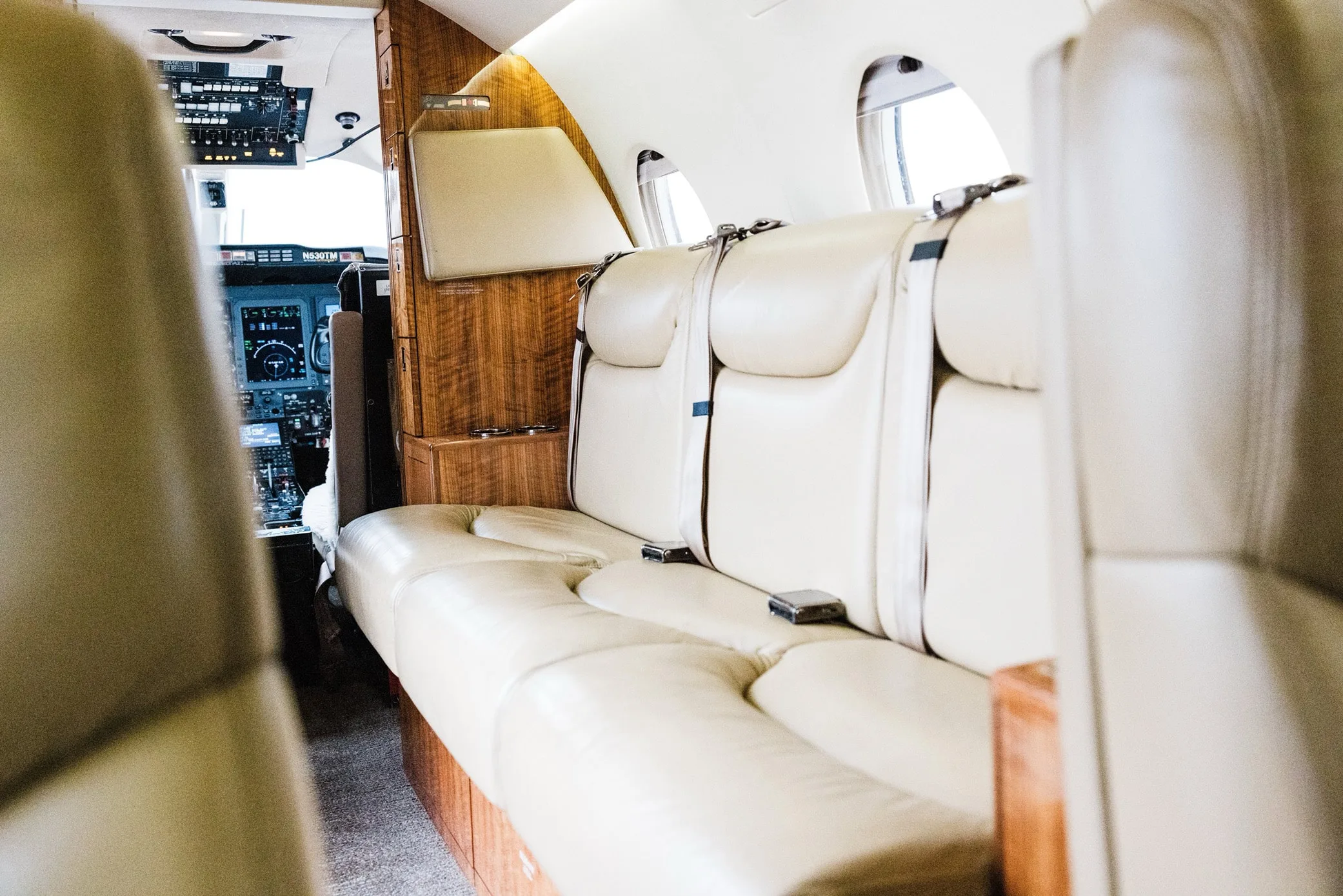 The luxurious beige leather seating in the private jet's cabin, with a glimpse of the cockpit.