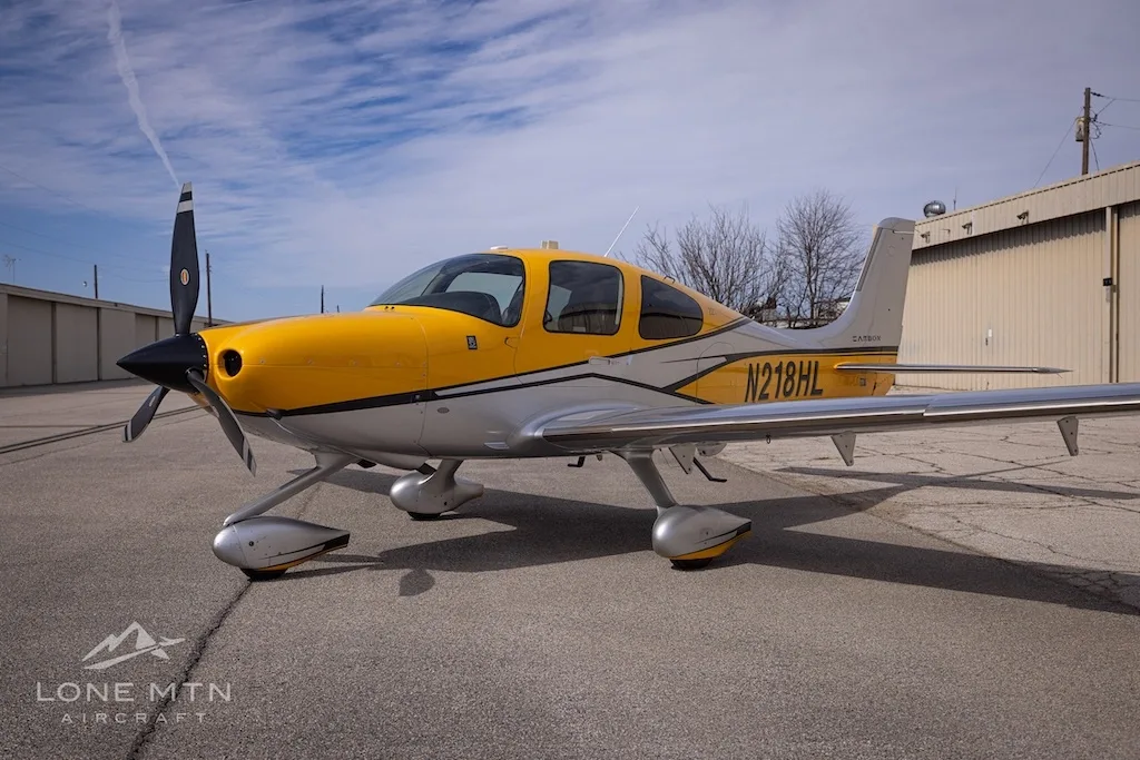 A Cirrus SR22 aircraft with yellow and silver paint scheme parked on an airfield, showing the front left.