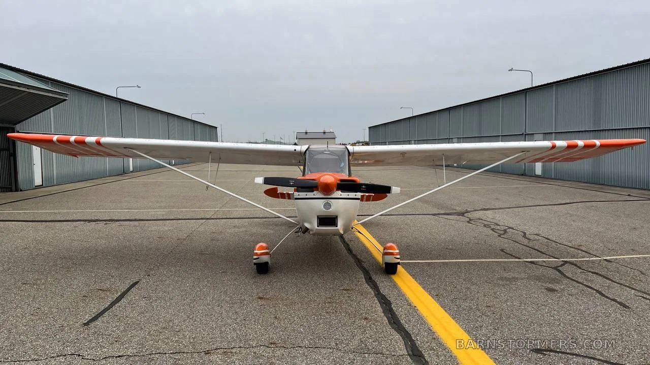 A head-on front view of an orange and white Cessna 170B aircraft with tail number N88319 parked on an asphalt apron.
