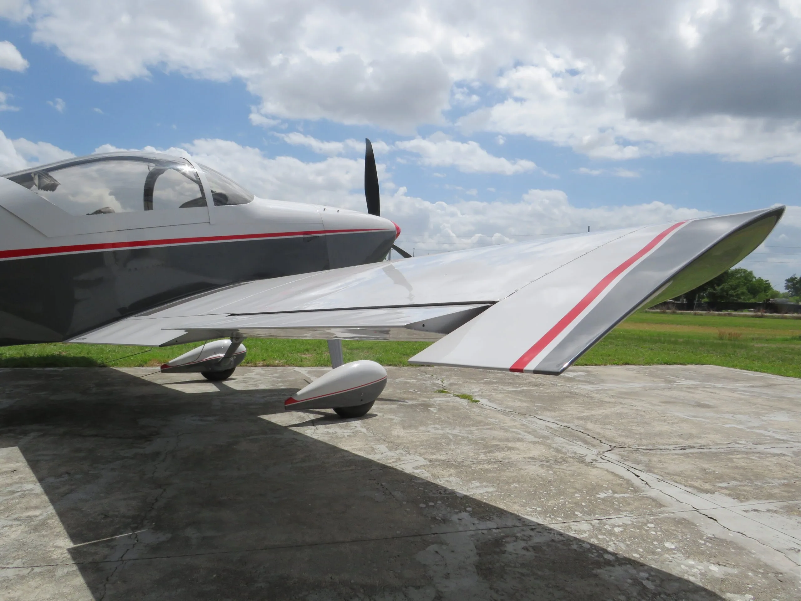 Side view of the wing and fuselage of a white and grey aircraft with red stripes, parked on concrete.