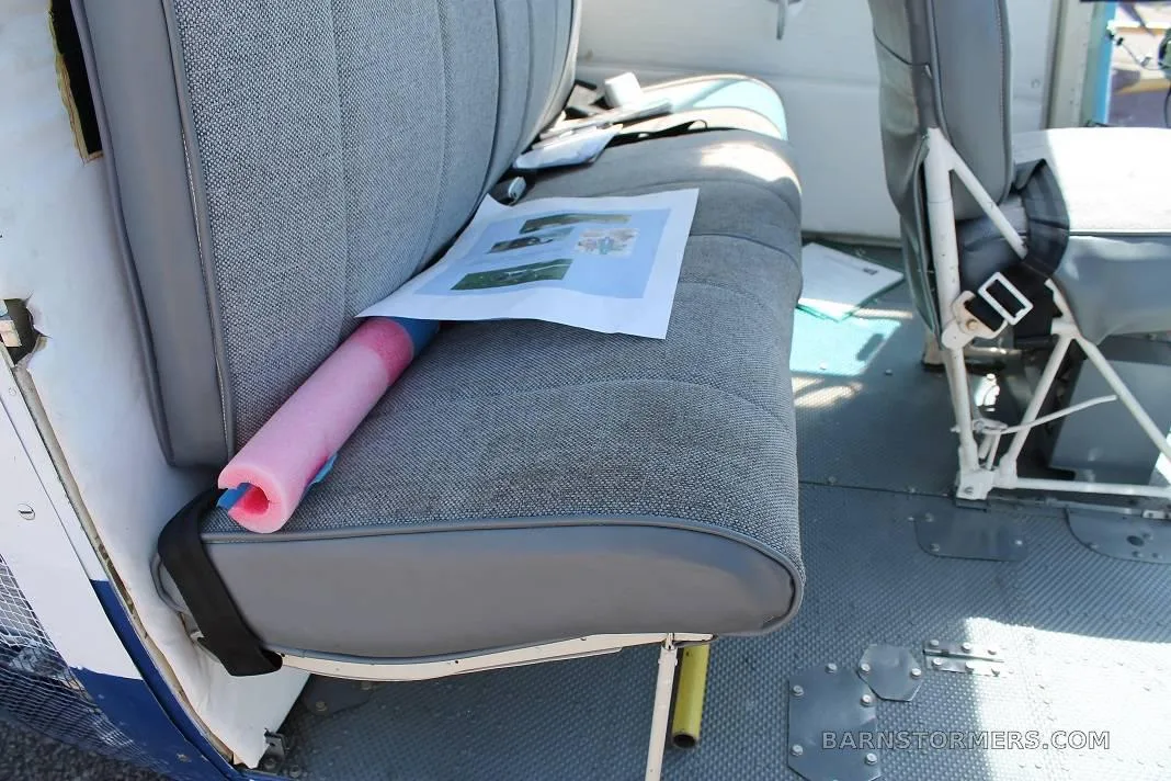 The grey fabric rear bench seat of a helicopter, with a document and a pink foam noodle on it.