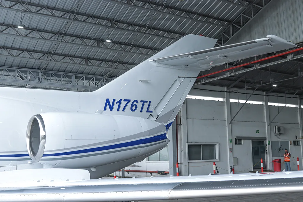 A rear-quarter view of the tail and engine of a white business jet with blue and grey stripes, registration N176TL, inside a hangar.