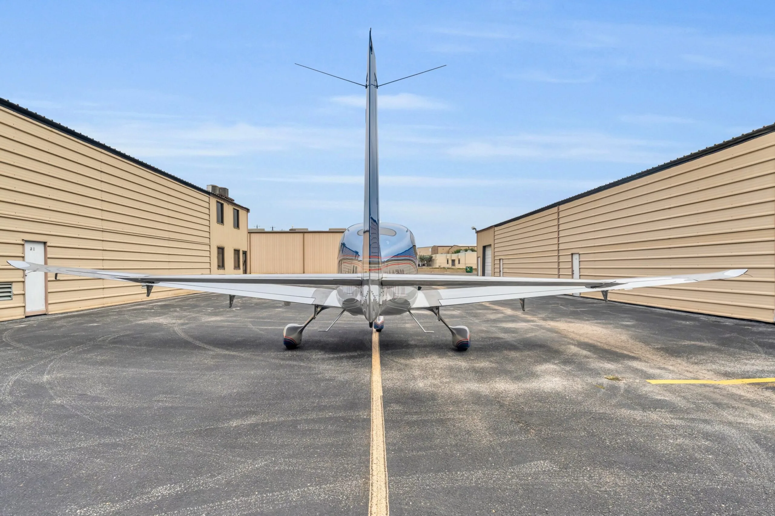 A rear view of the blue and silver Cirrus SR22T GTS aircraft N66TM, centered on an asphalt taxiway between hangars.