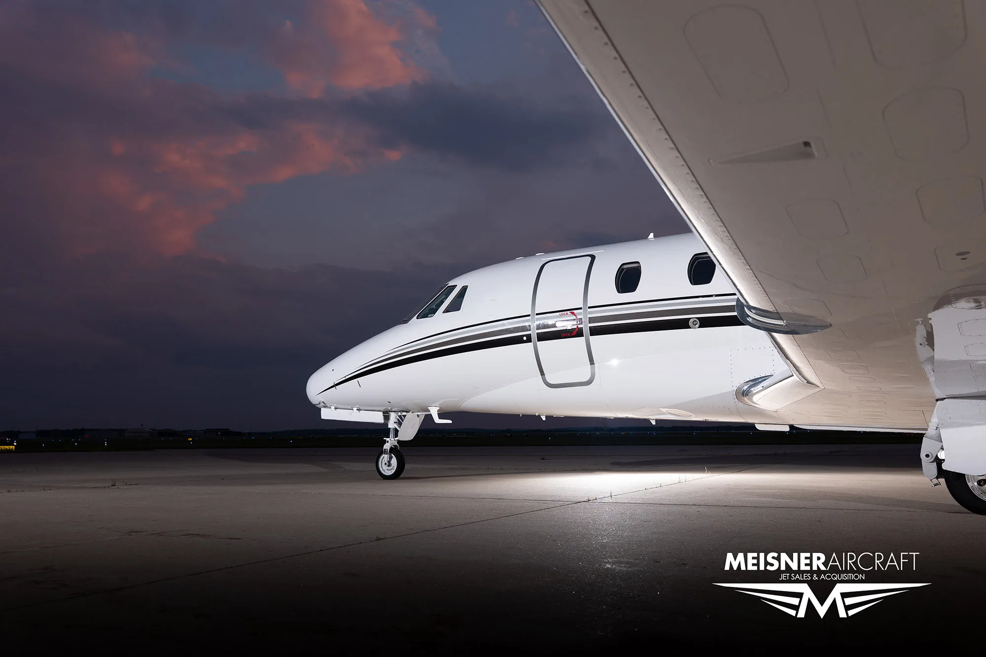 A close-up view of the front fuselage and wing of a white Citation Excel business jet on a tarmac at dusk.