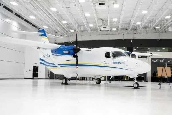 A white and blue Kamaka Air aircraft with twin propellers is parked inside a brightly lit hangar.