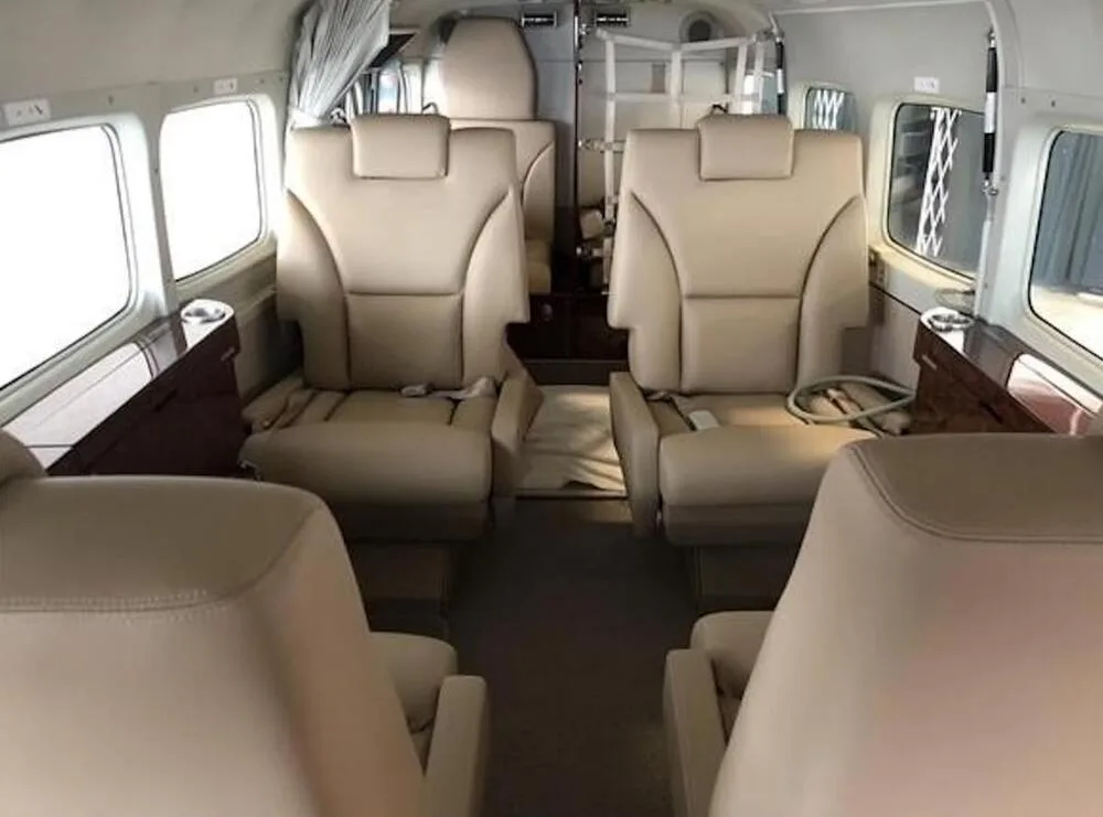 The aircraft cabin interior with multiple rows of tan leather seats and wood-paneled side consoles.