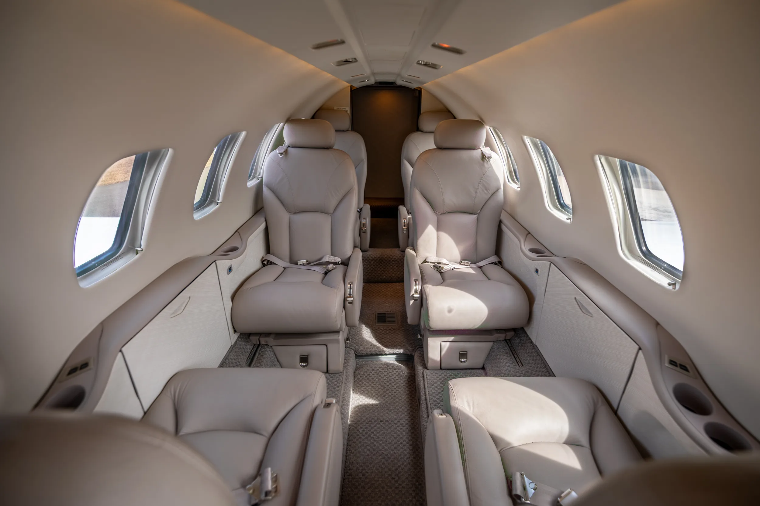 The luxurious beige leather cabin interior of a Cessna Citation Excel, showing rows of passenger seats.