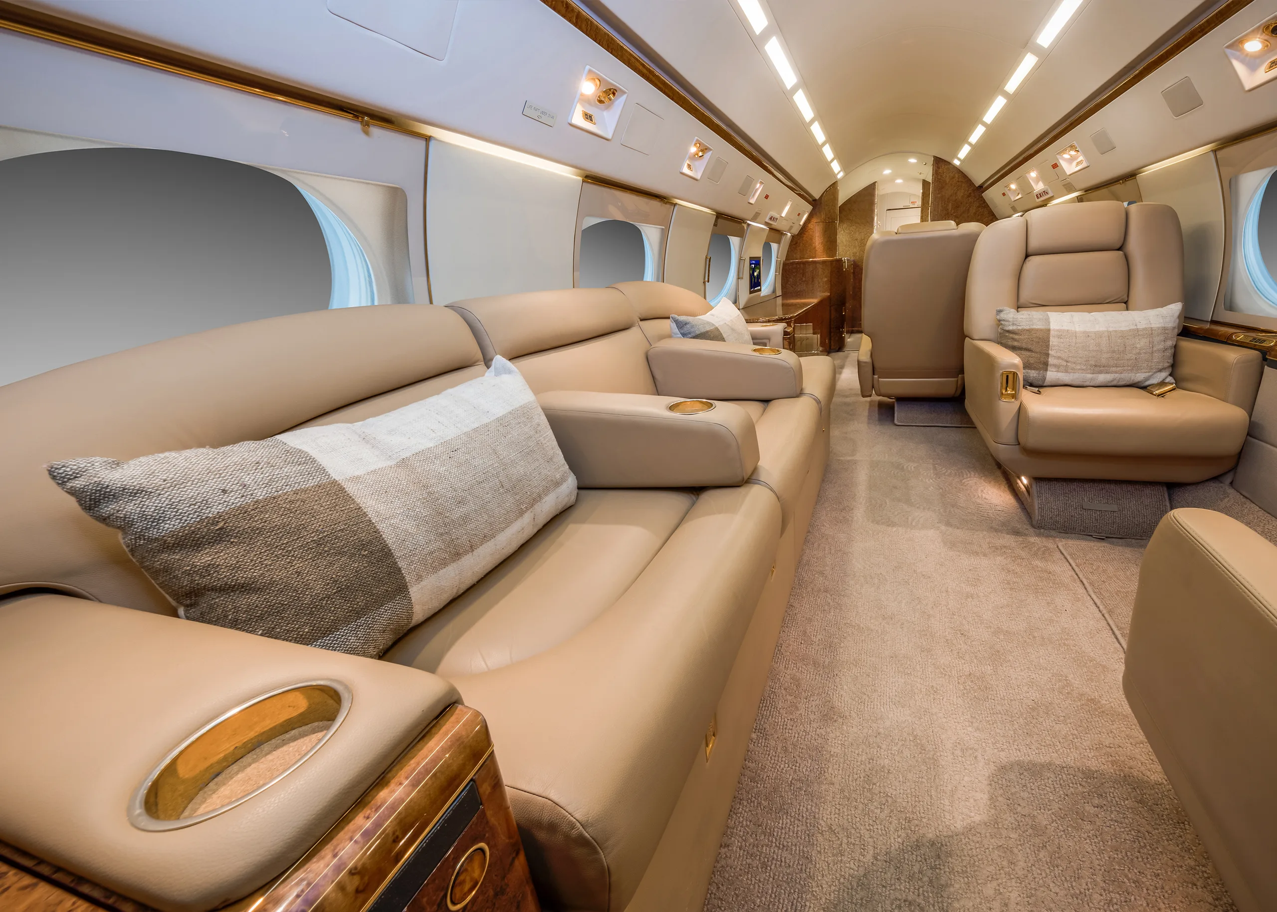 A wide shot of a luxurious aircraft cabin featuring a long beige leather sofa and individual seats.