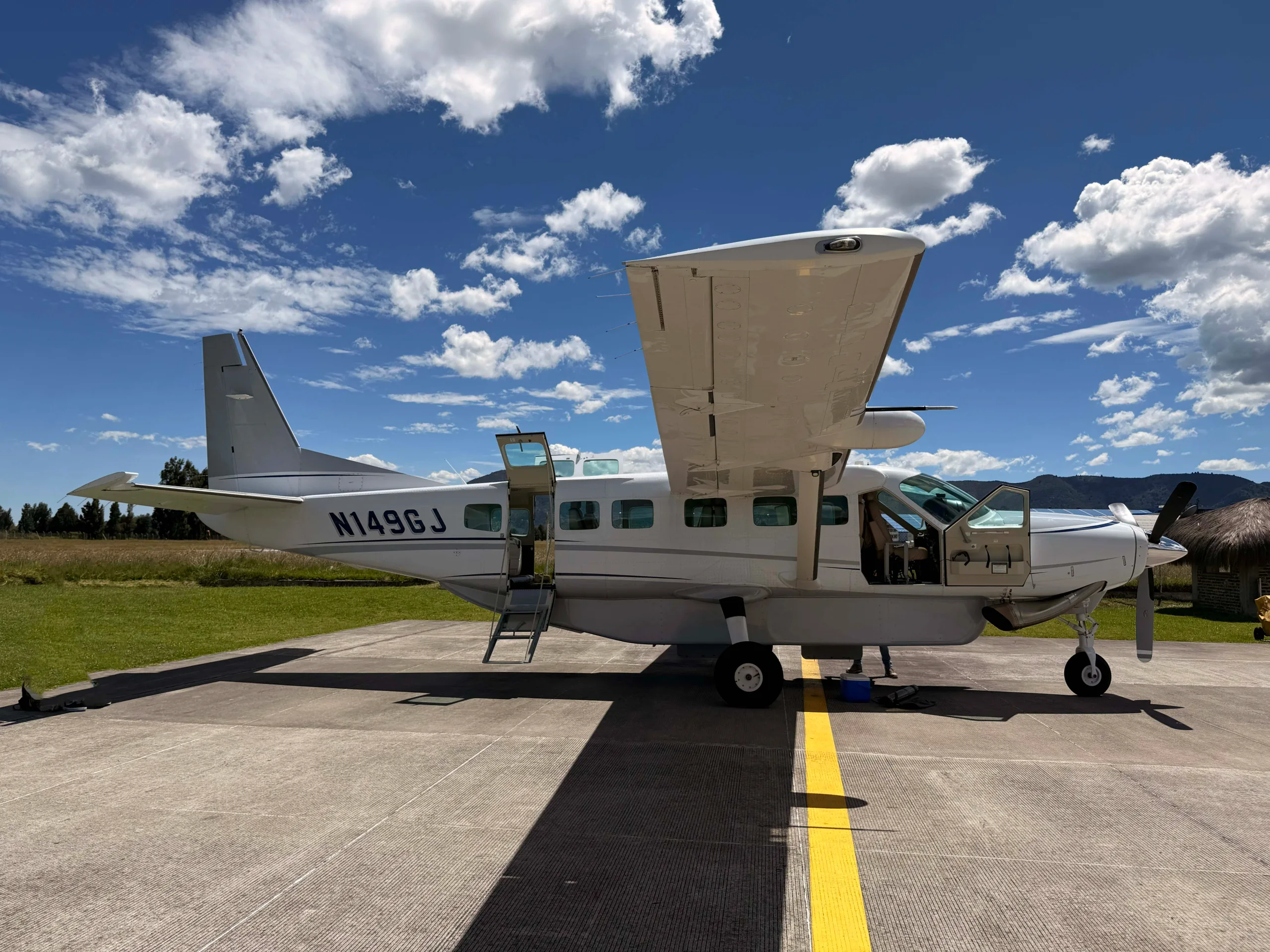 A white Cessna Caravan N149GJ with open doors and a ladder parked on an airfield.