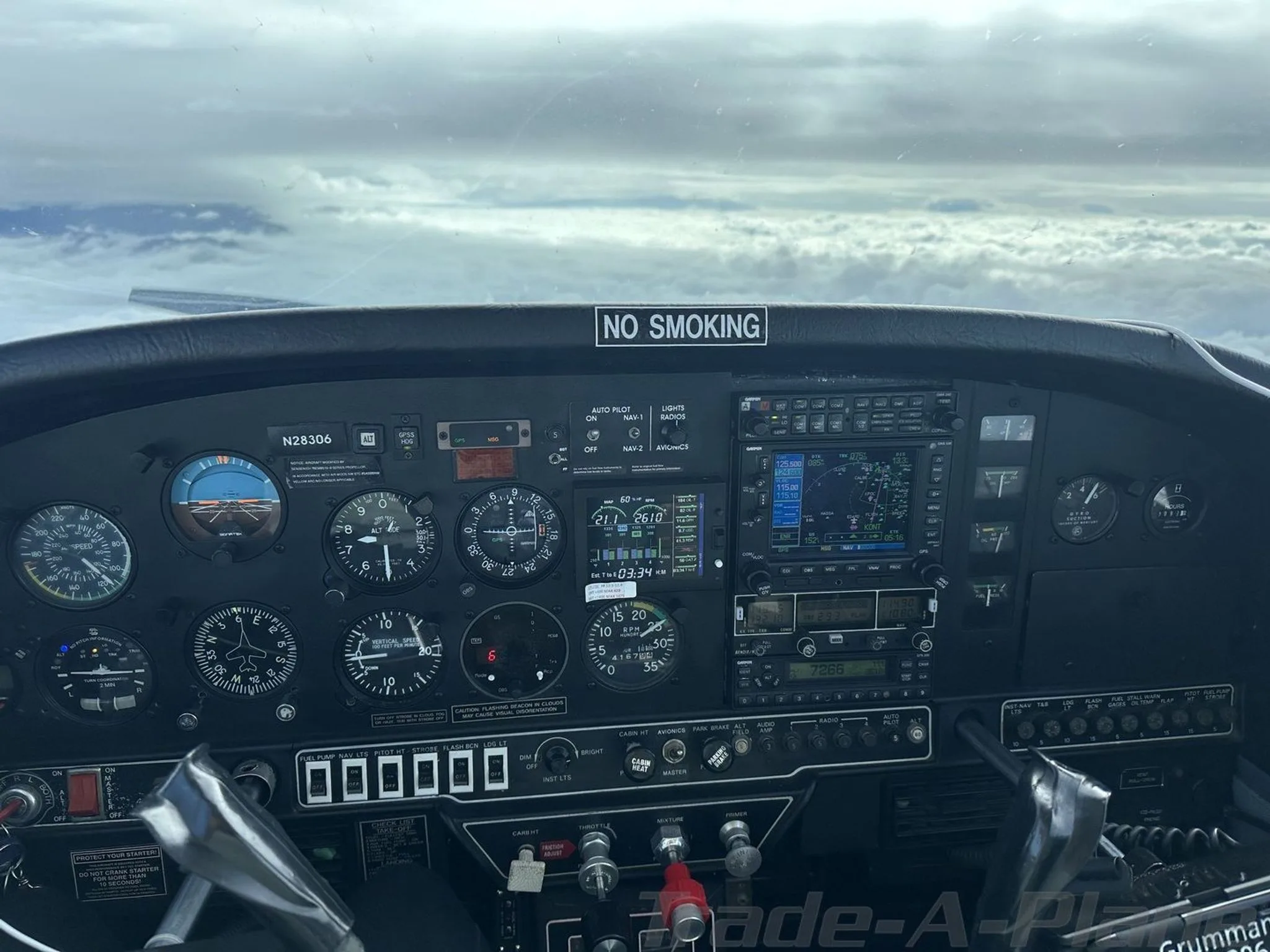 The instrument panel of the Grumman AA5B Tiger, N28306, showing gauges and avionics with clouds outside.