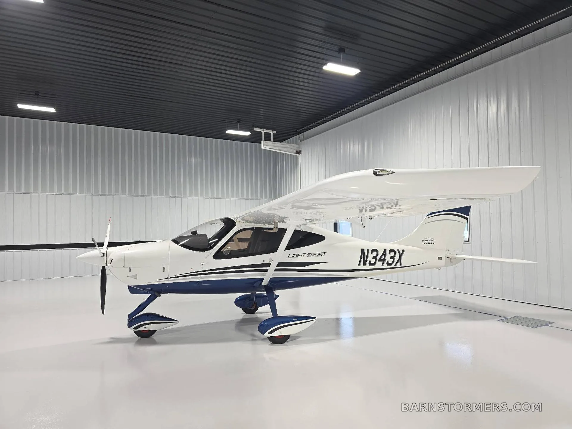 A white Tecnam P2008 Light Sport aircraft with blue accents, registration N343X, parked in a clean hangar.